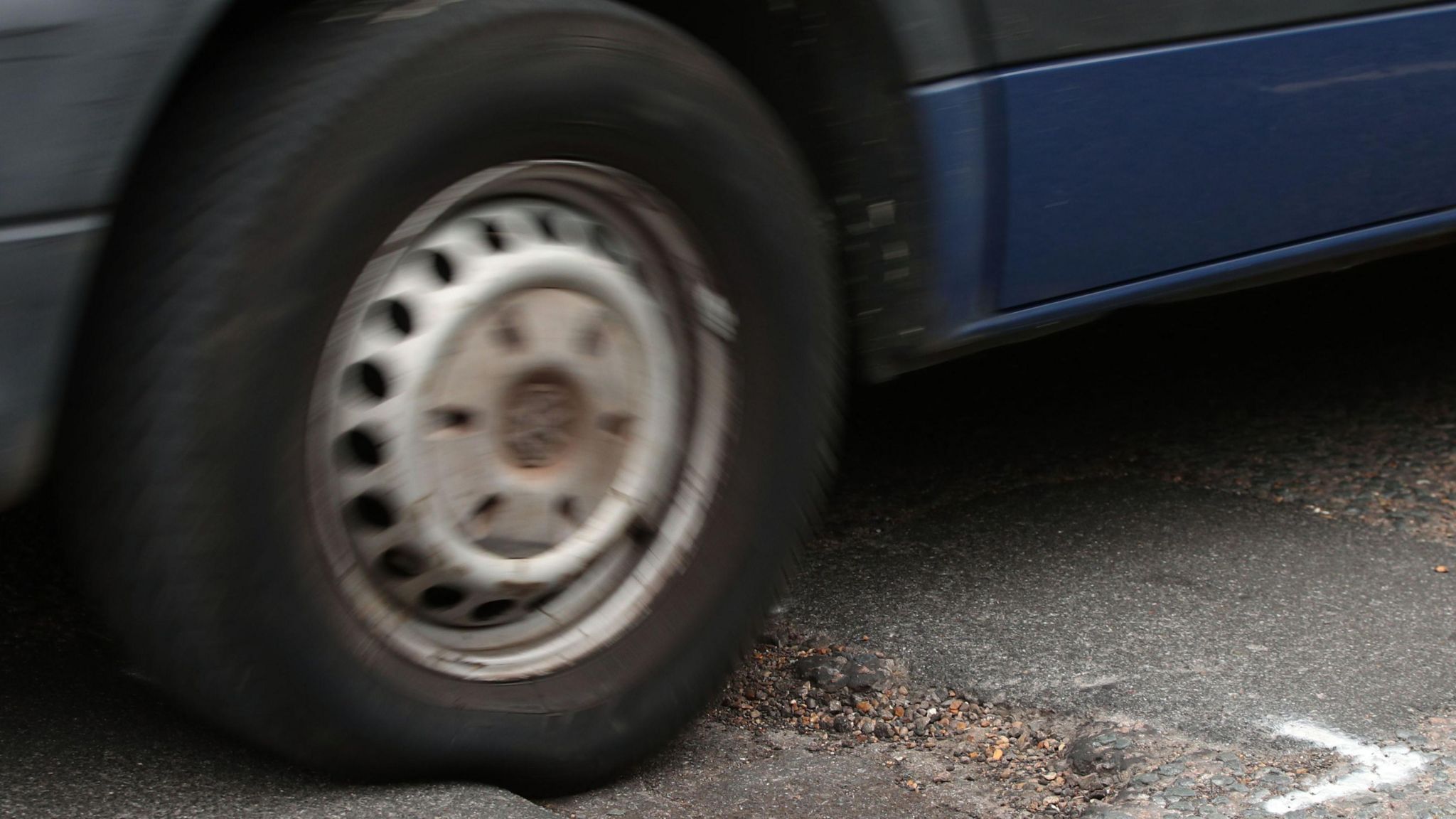 A car tyre drives over damage on a road