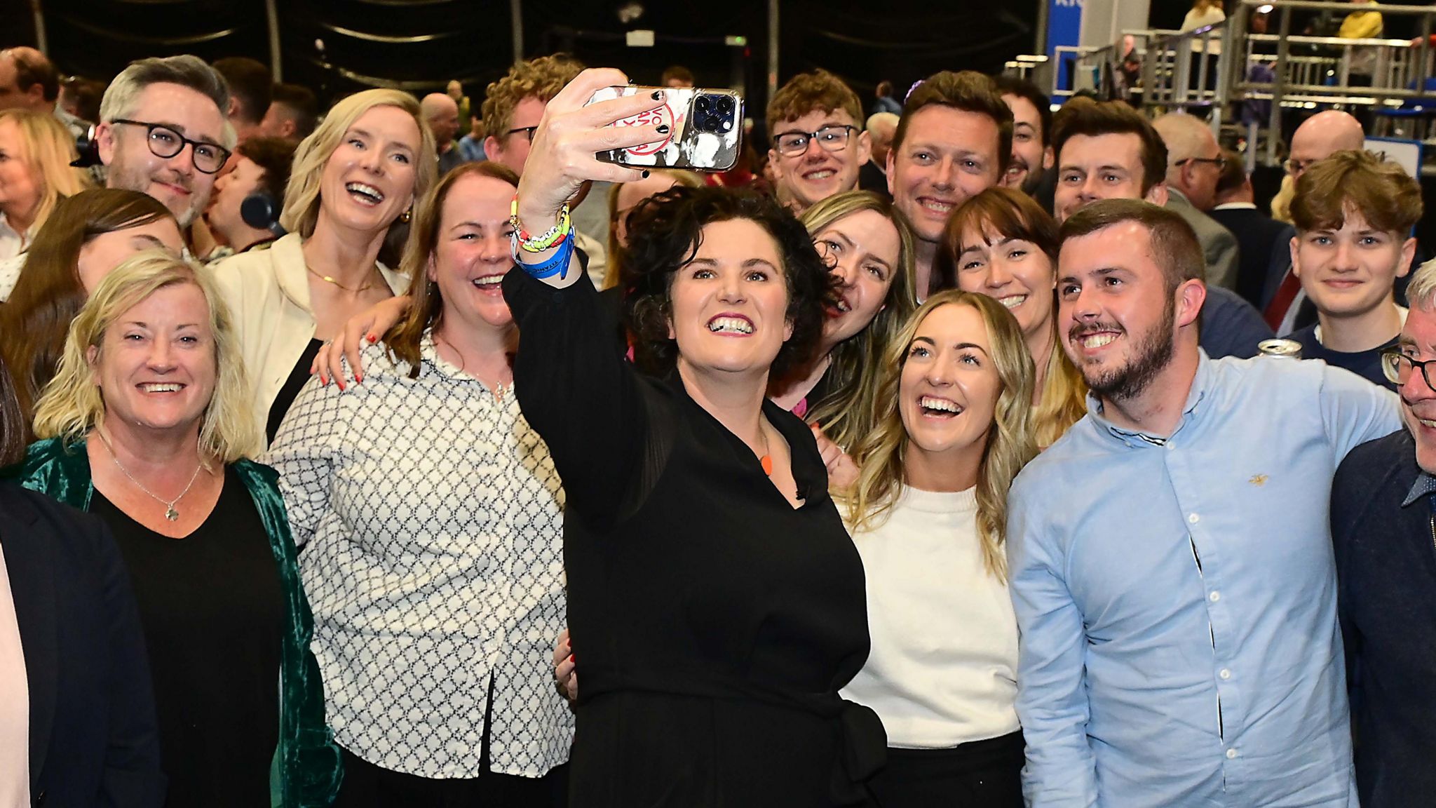 A smiling Claire Hanna takes a selfie while surrounded by ecstatic supporters