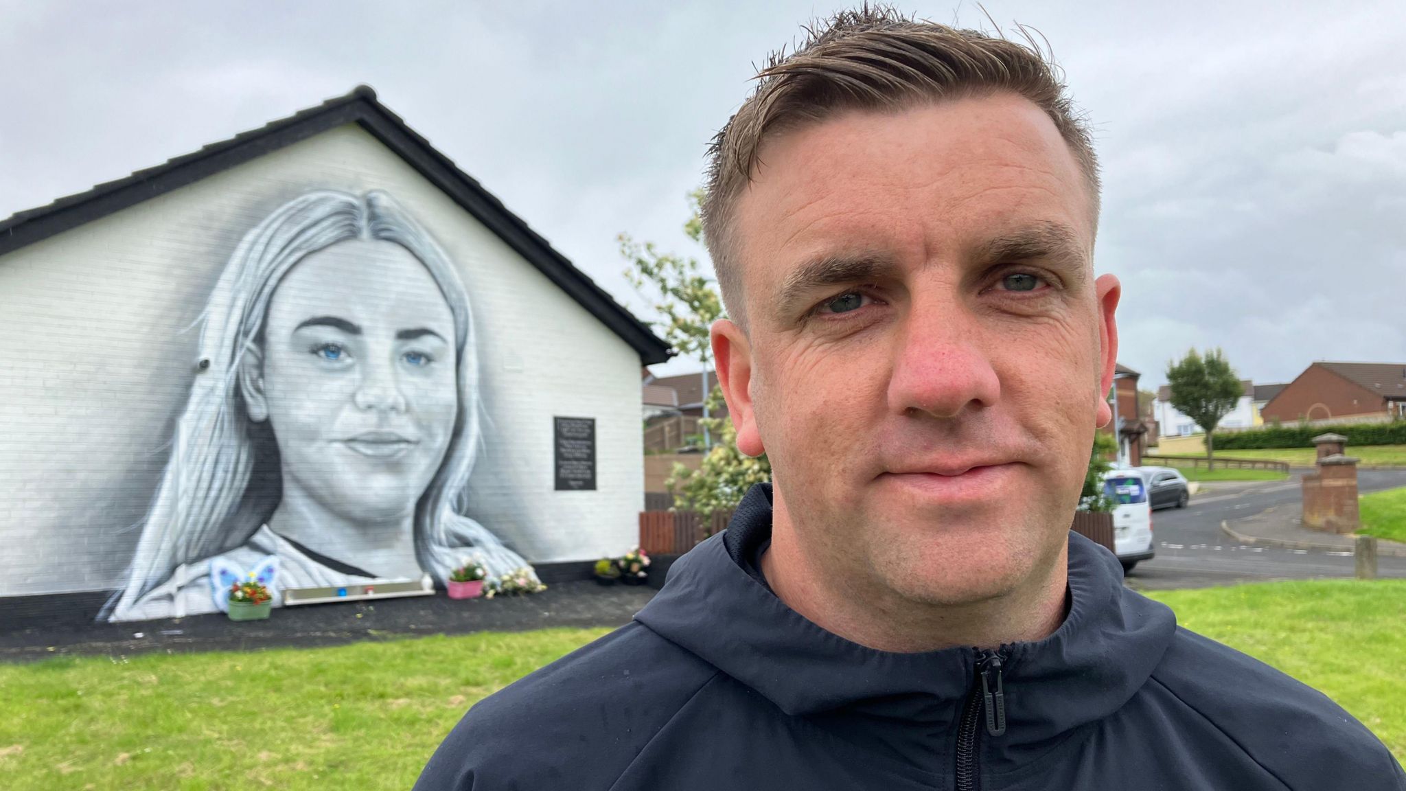 Mo Mahon standing in foreground with mural of his niece Caitlin mcLaughlin in the background
