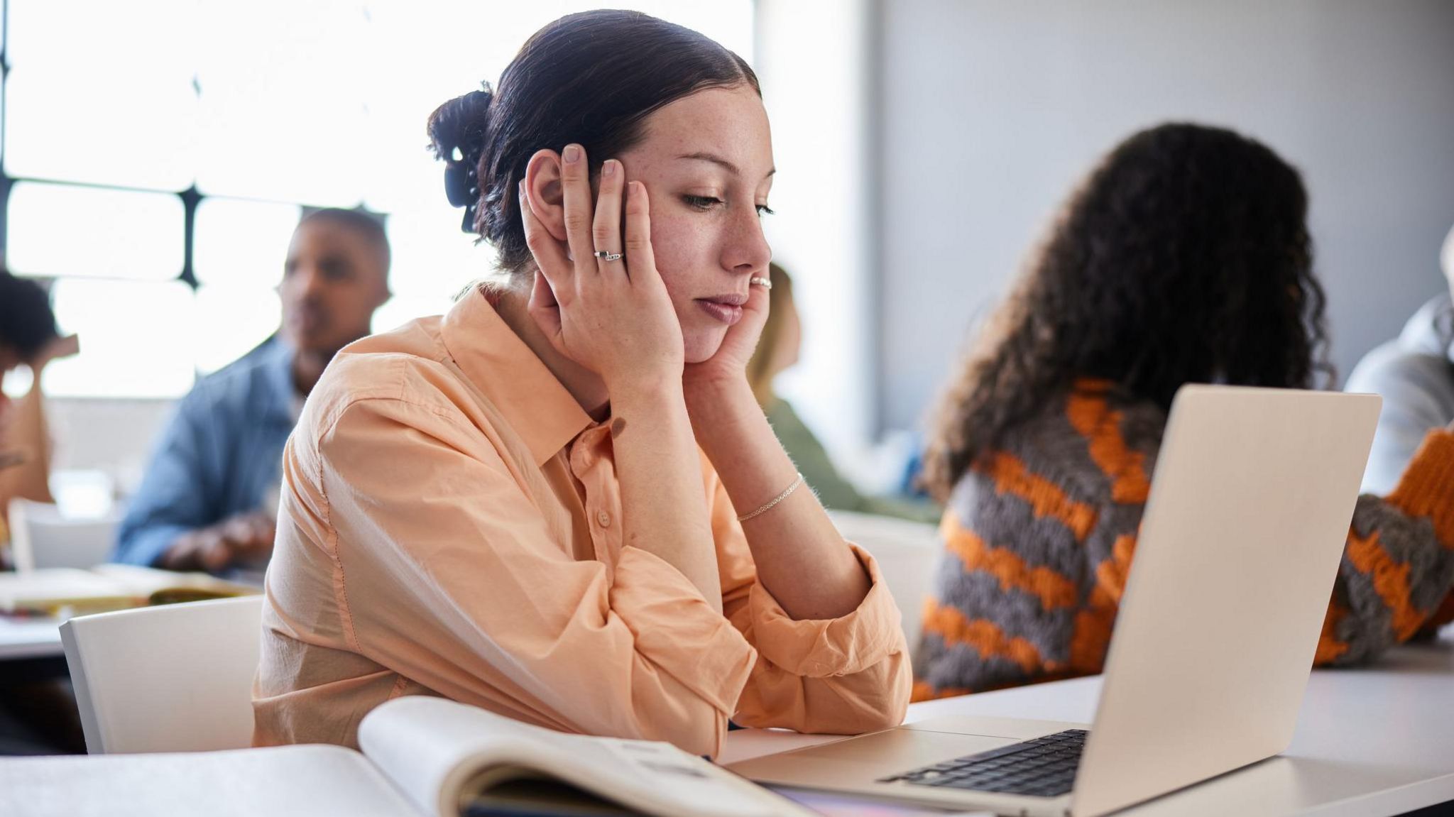 A woman looking at a laptop computer with her hands on her cheeks, looking fed-up