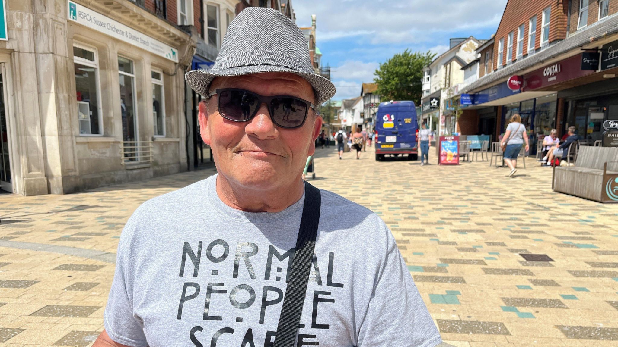 Roger Stevens stands in the town centre wearing a trilby hat and t-shirt