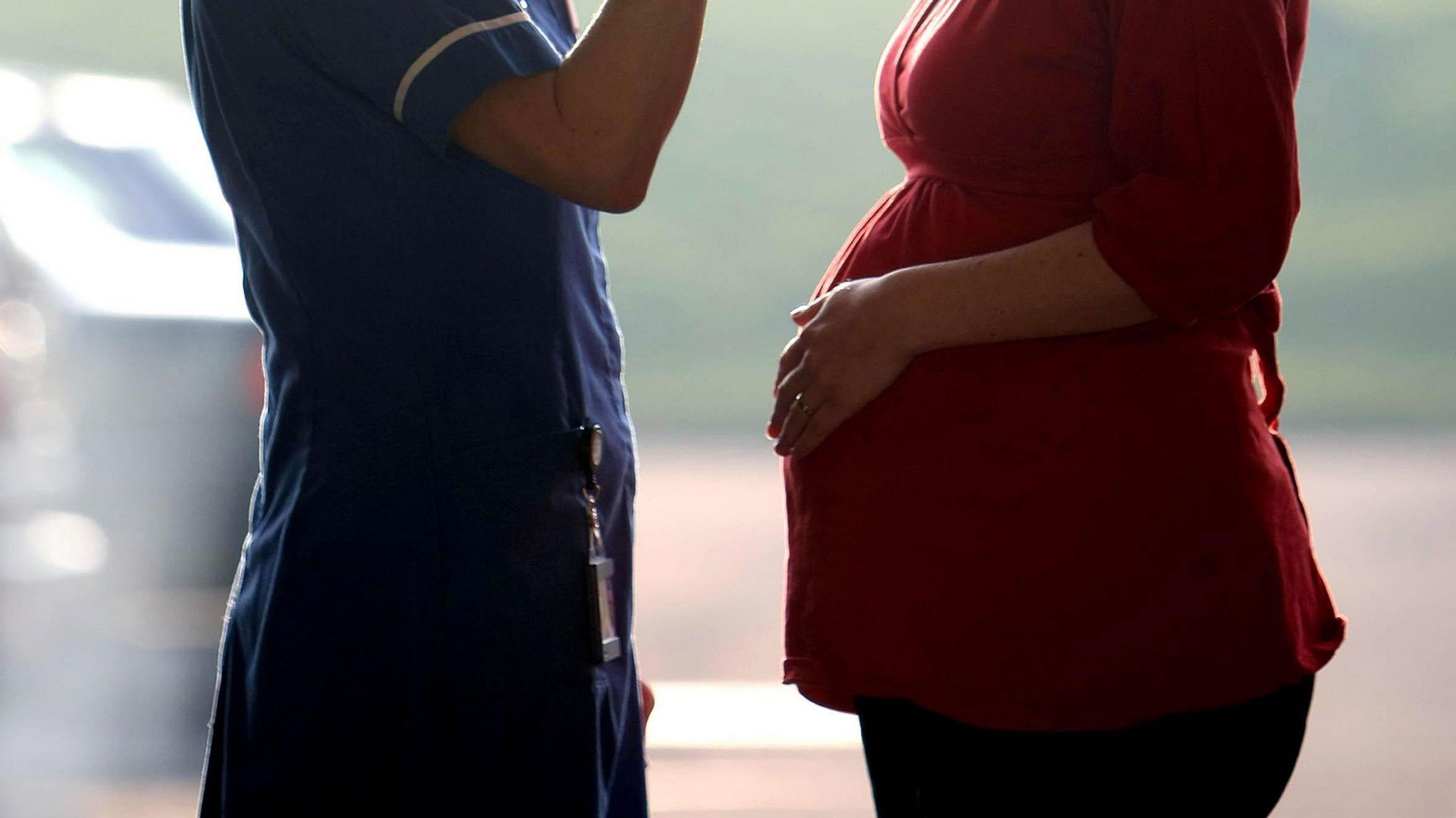 A pregnant woman wearing a red blouse, standing in front of a nurse