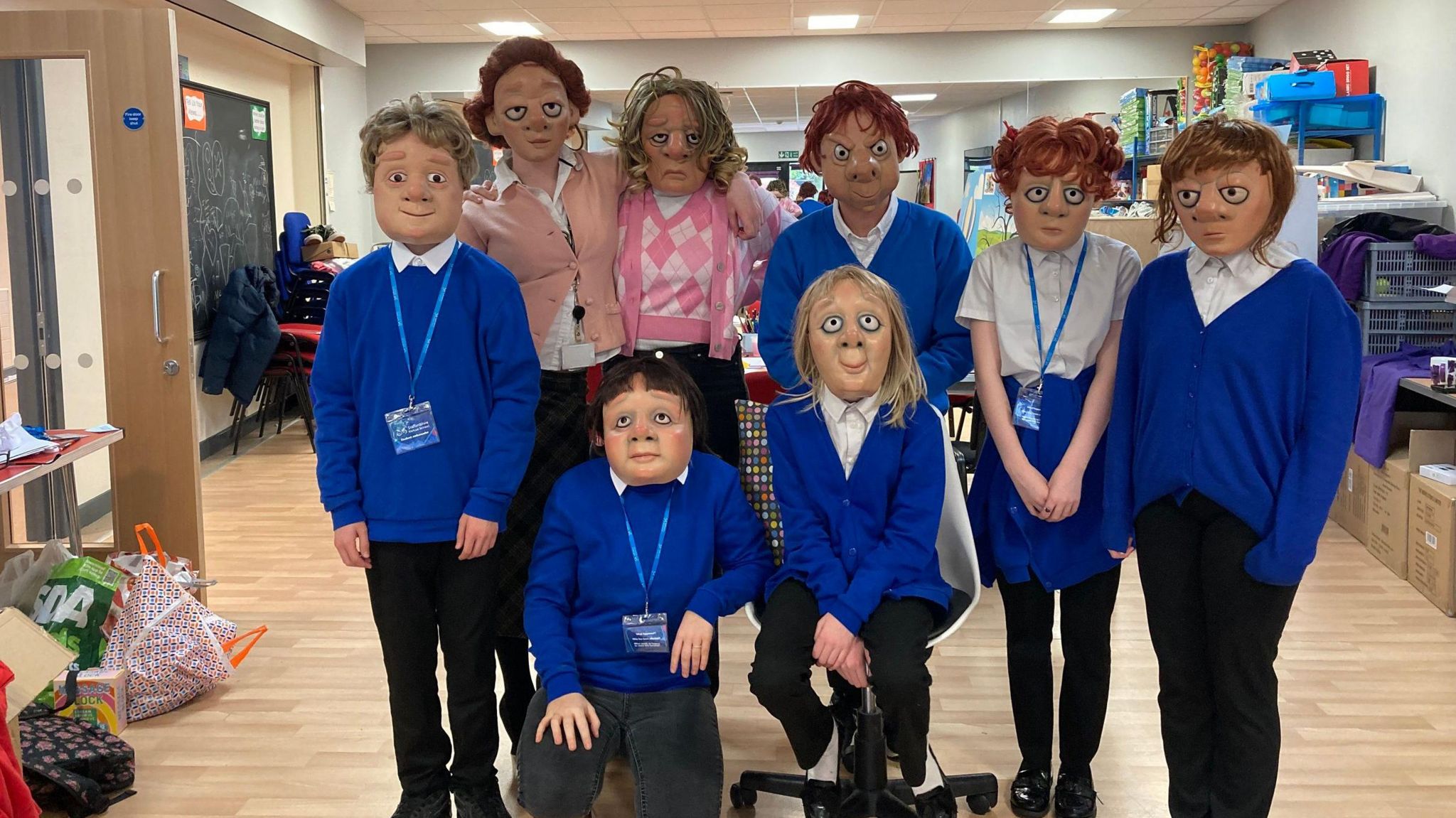 Children dressed in blue cardigans and white school shirts while wearing masks and synthetic wigs