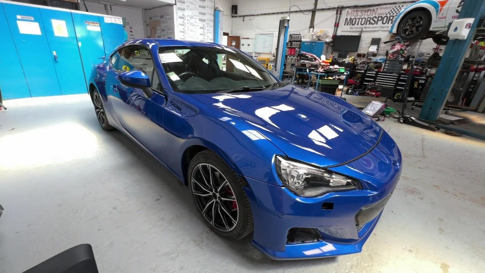 A blue 2016 Subaru BRZ in the Mission Motorsport workshop. The car has no visible damage and looks as good as new.