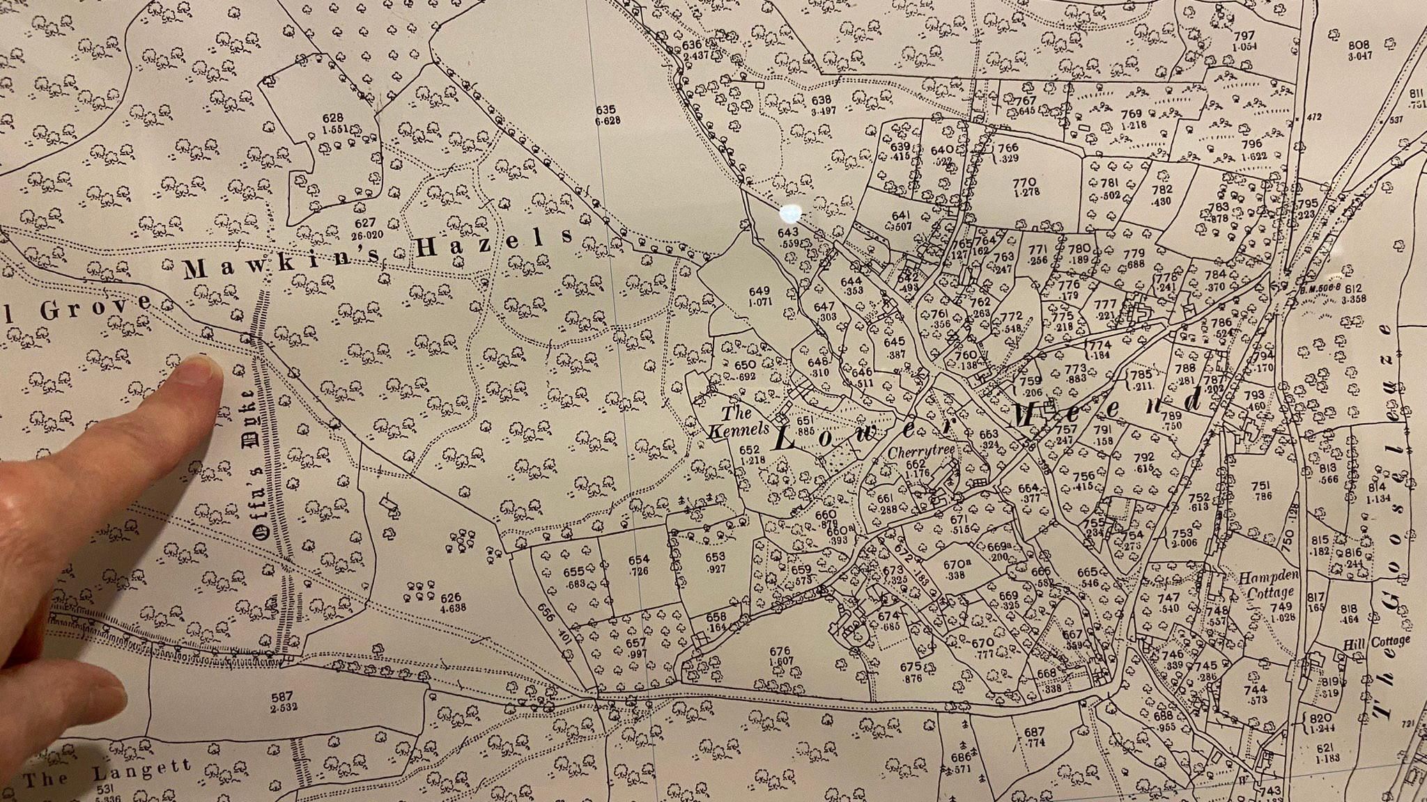 A finger pointing at a location among trees on an old map