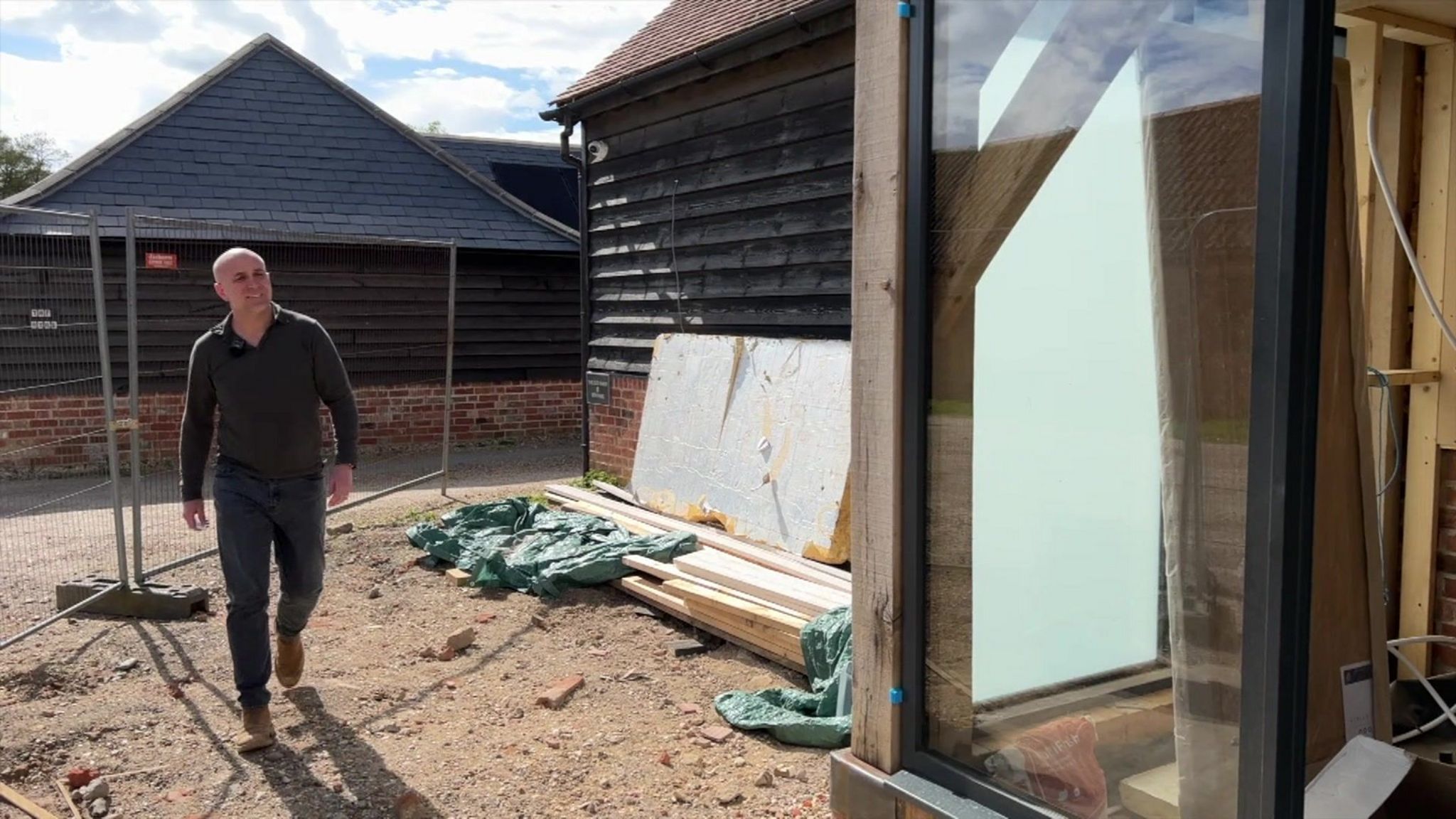 Joe Atkinson walking towards his property, which is under renovation, and has a metal gate around it 