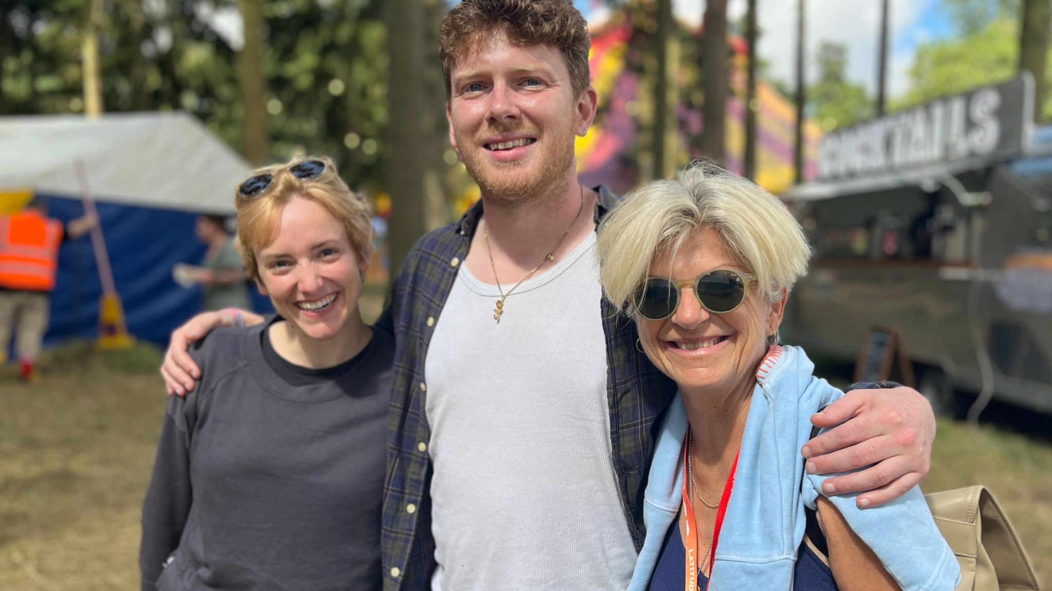 Actors Charlie Cameron and Joe McArdle with INK director Julia Sowerbutts stand together in front of festival tents