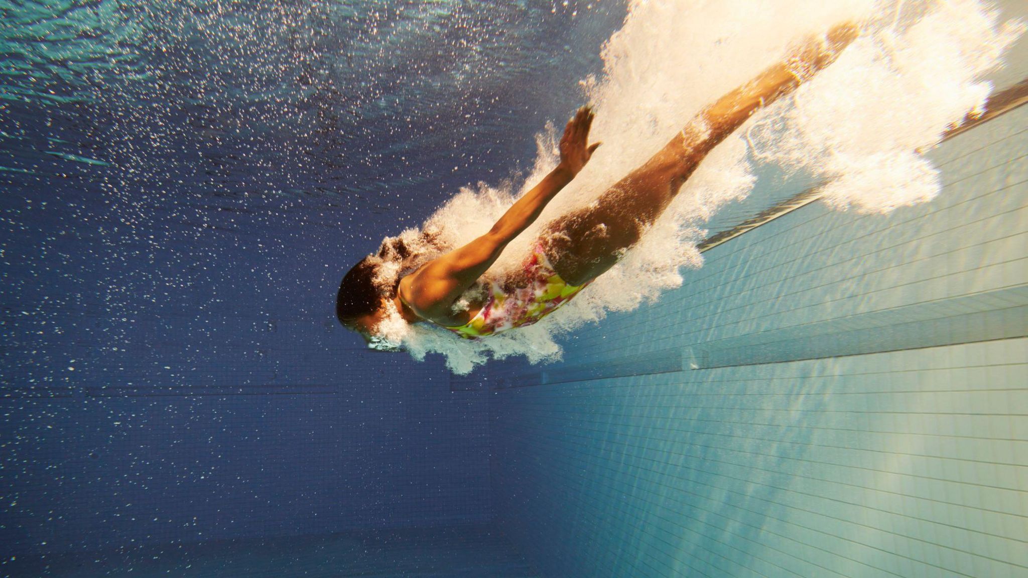 A woman in a yellow and pink swimming costume diving underwater