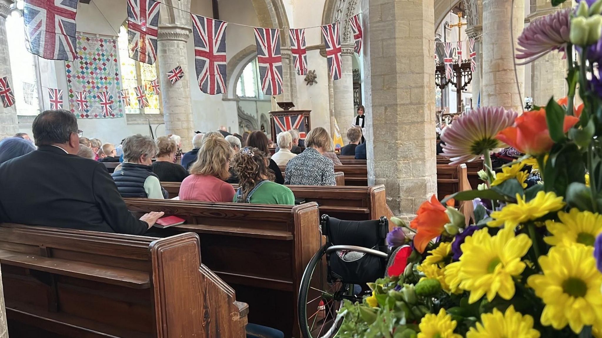 Interior of St Andrew's, Soham, showing people sitting in pews and Union Flags hanging in lines above