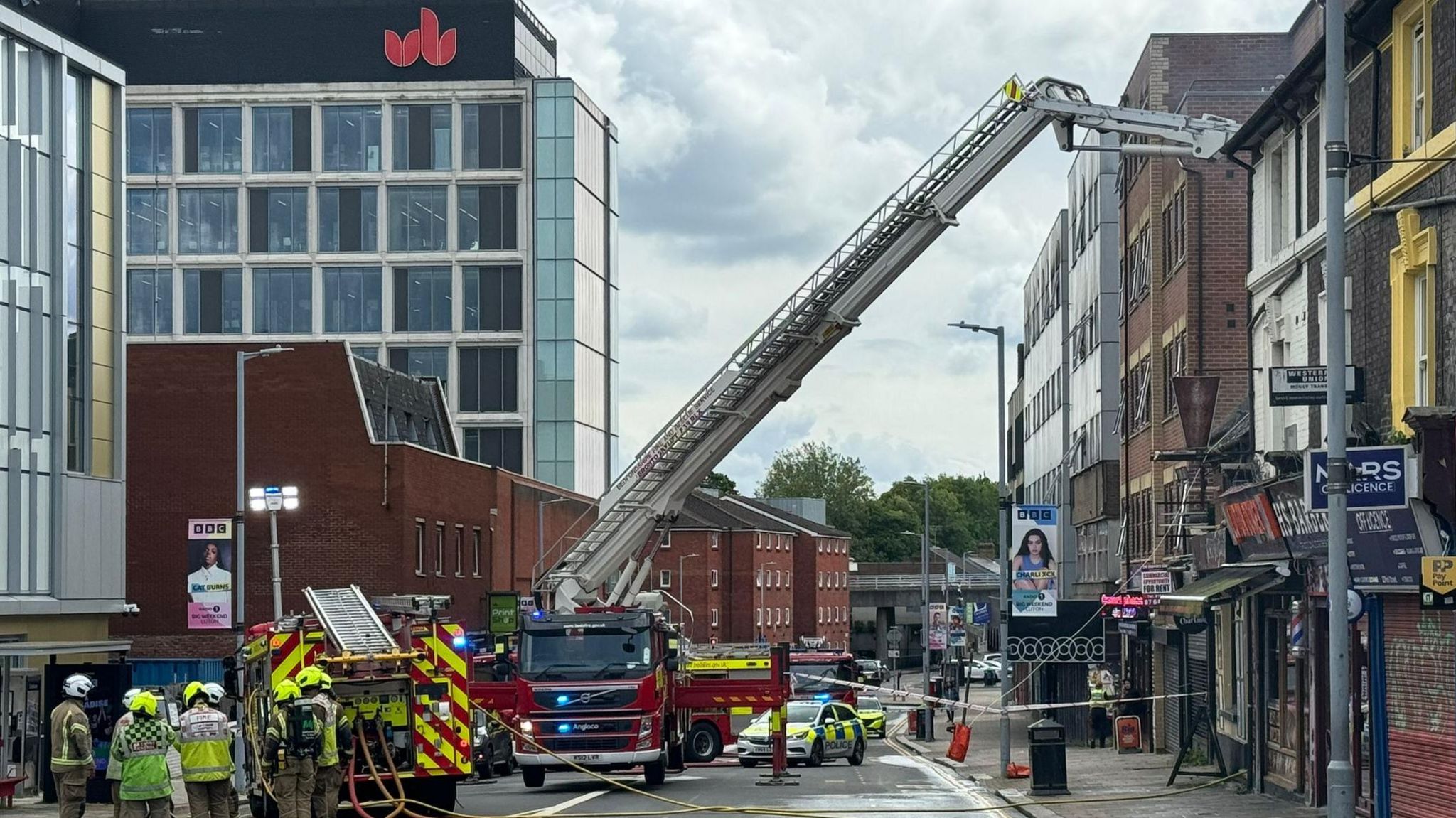 Fire engines, hydraulic ladder and crews outside building on fire 