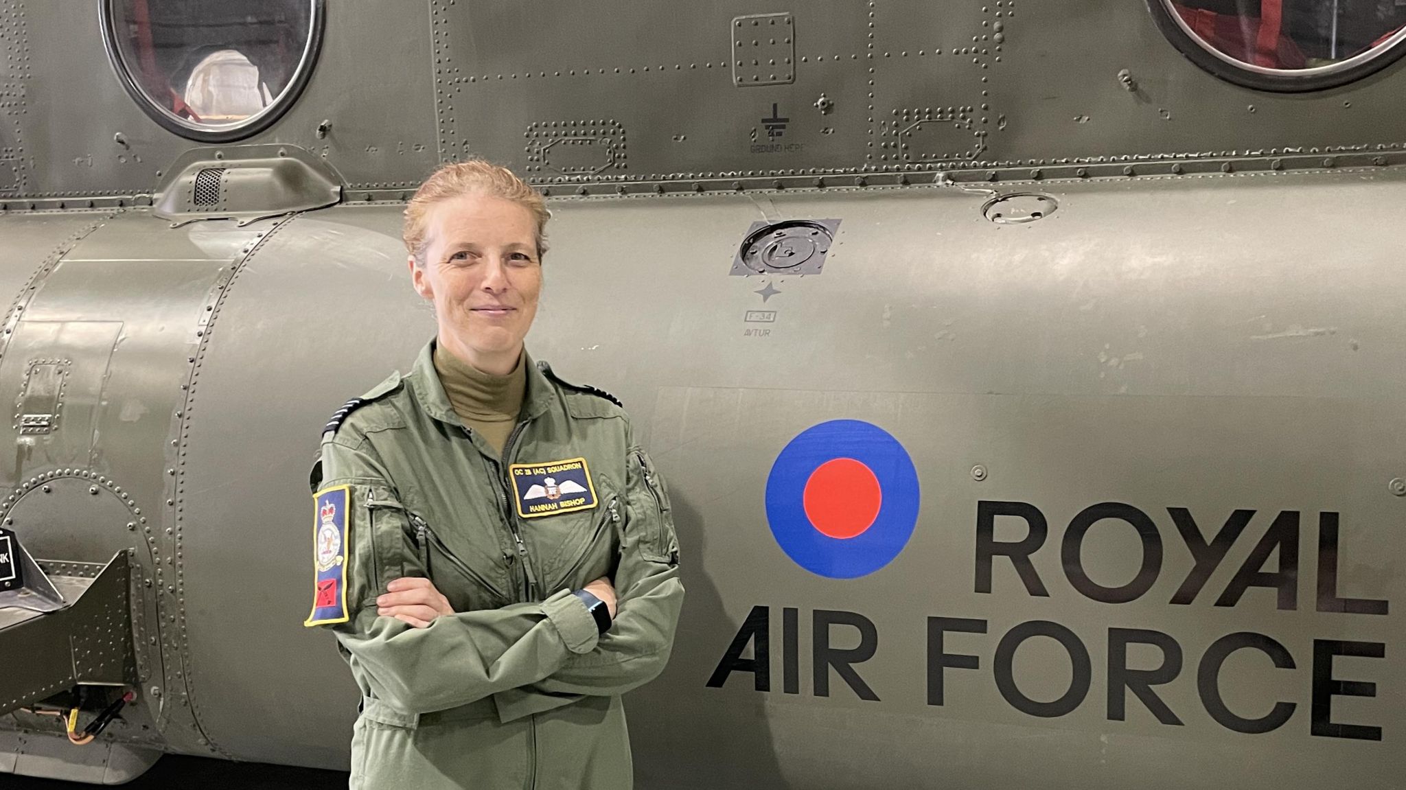 Wing Commander Hannah Bishop in flight suit in front of a Chinook helicopter with the RAF insignia behind her on the aircraft