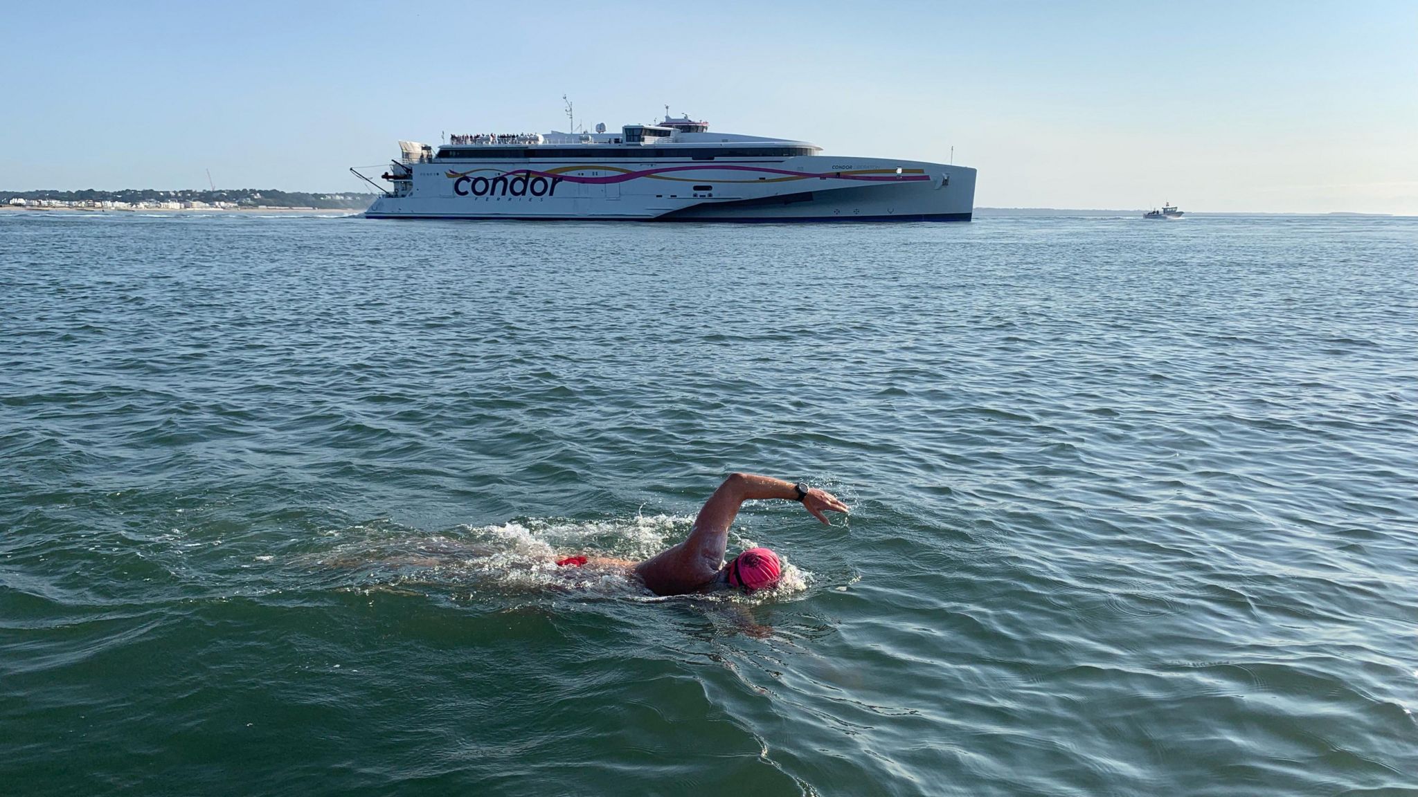 A man wearing a swim cap swimming in the sea, with a large boat in the background