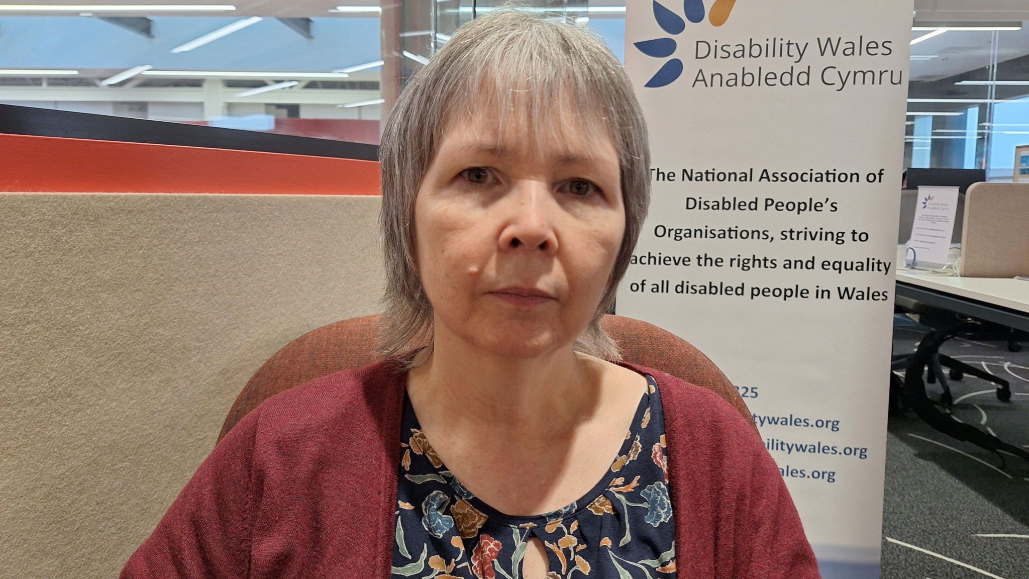 Rhian Davies looking into the camera in front of a Disability Wales banner.