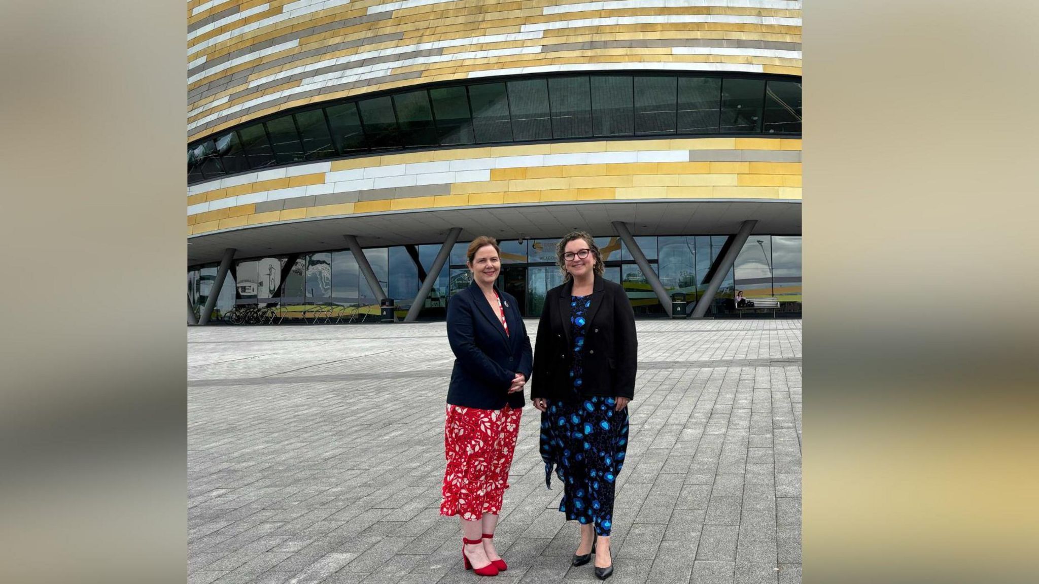 Two women standing outside the gold, silver and bronze-coloured Derby Arena