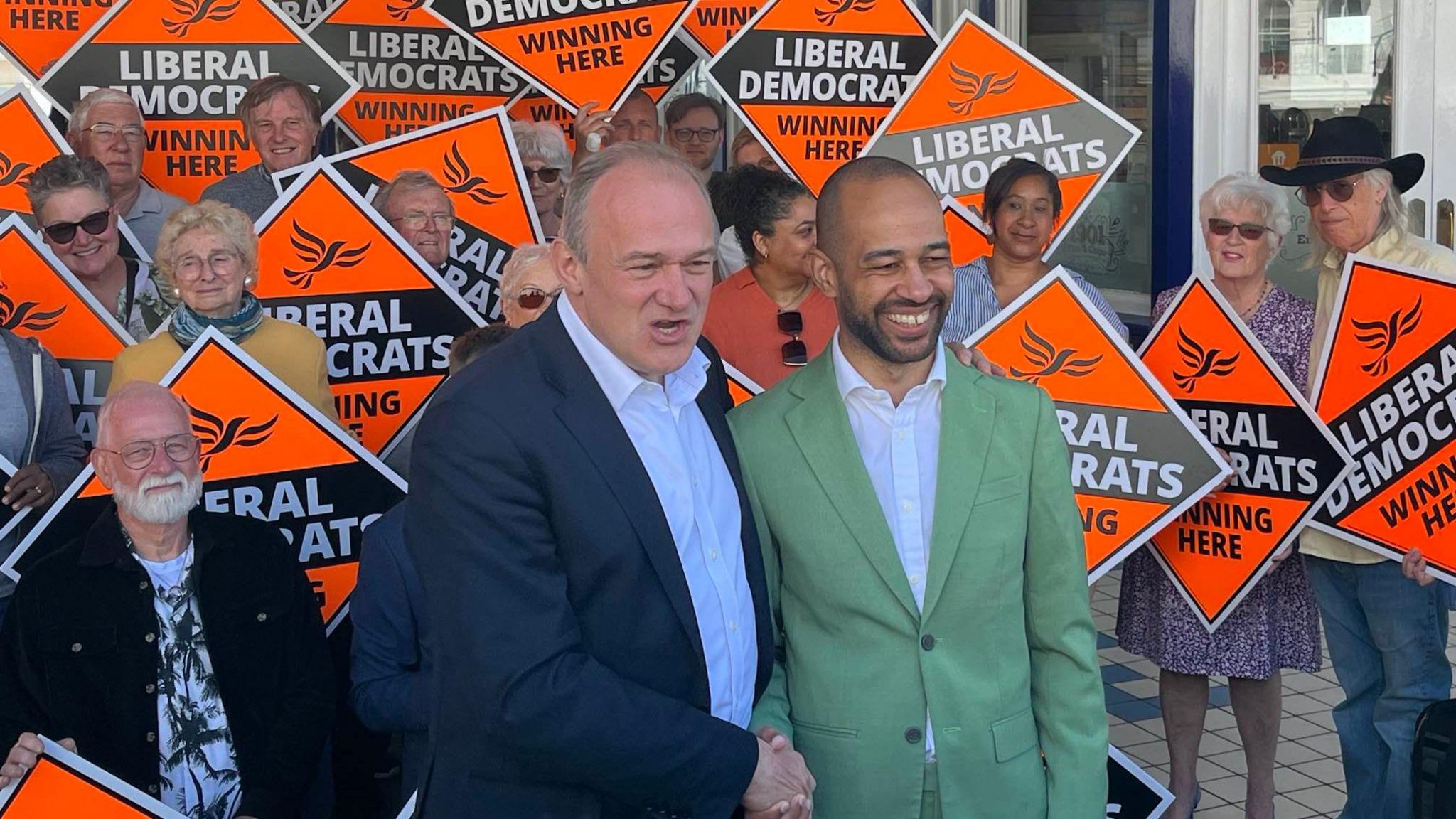 Sir Ed Davey and Josh Babarinde with a group of Liberal Democrat supporters holding up party signs