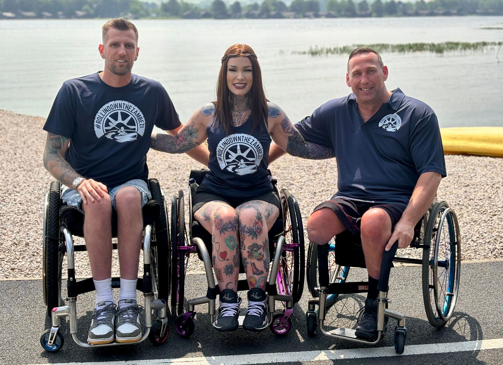 The three paddlers sitting in their wheelchairs on the shore while linking arms