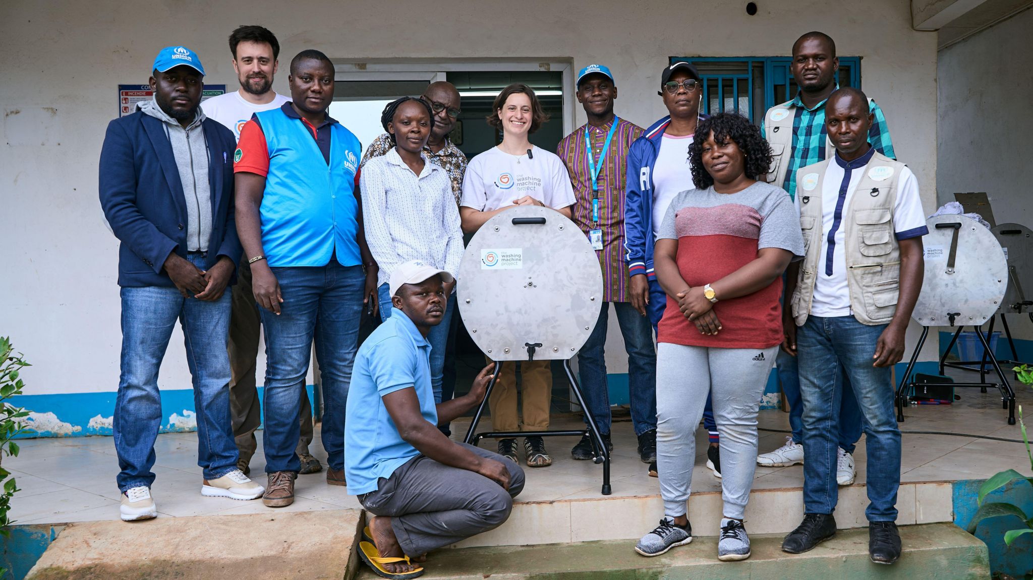 A group of mainly Congolese people pose around a manual washing machine.