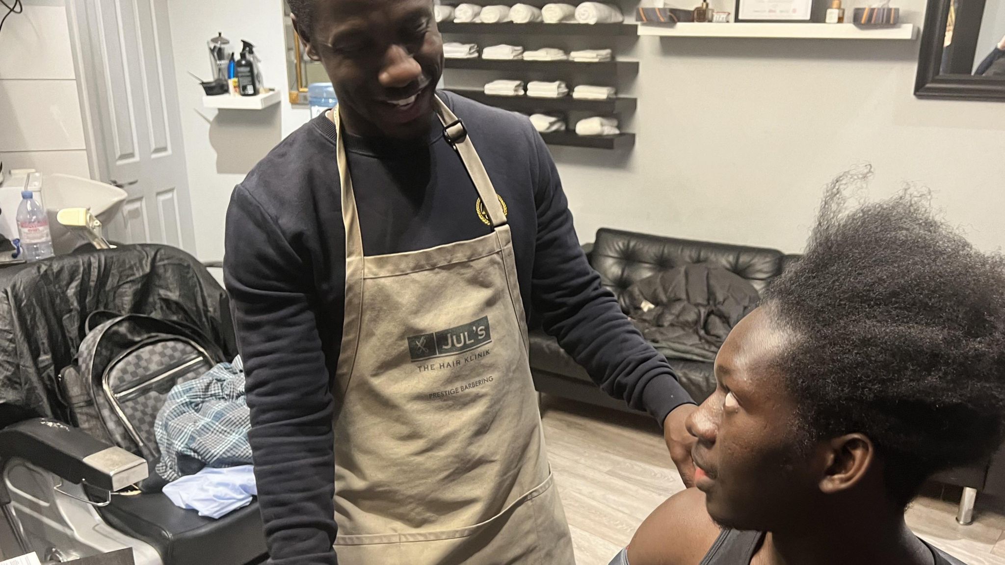 A staff member at Jul's barber shop in south London looks at a customer while testing his blood pressure with an out-of-shot machine that has a cuff