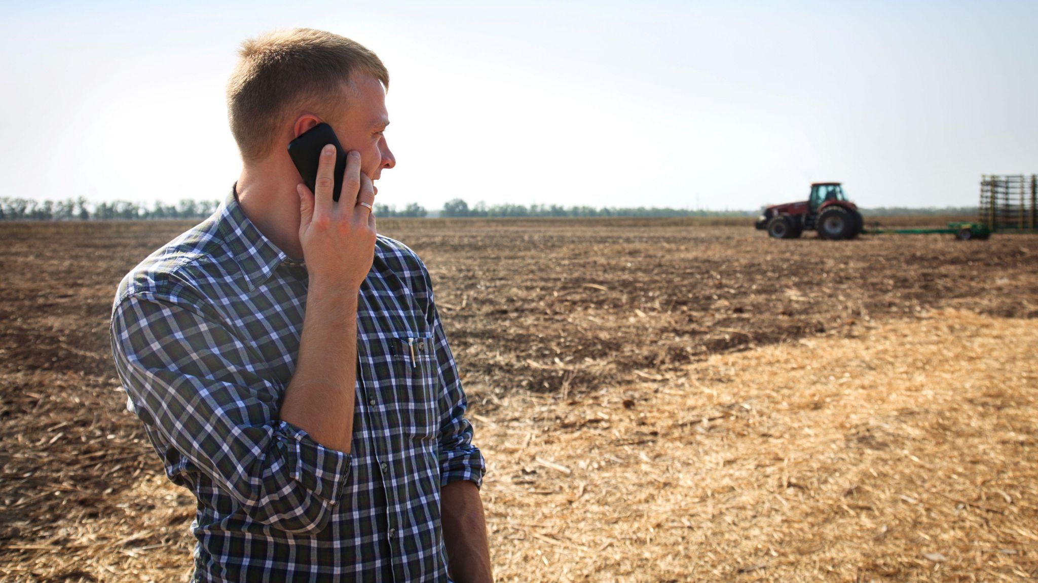 Man on a mobile phone in a field with a tractor