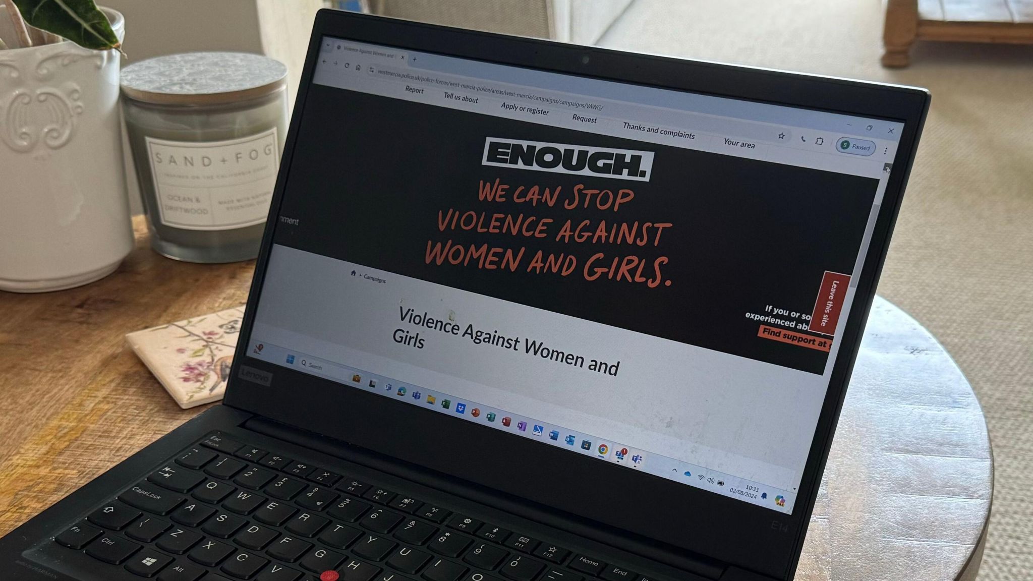 An open laptop with a website on its screen that reads "Enough, we can stop violence against women and girls". The laptop is resting on a wooden table and there are ornaments behind it