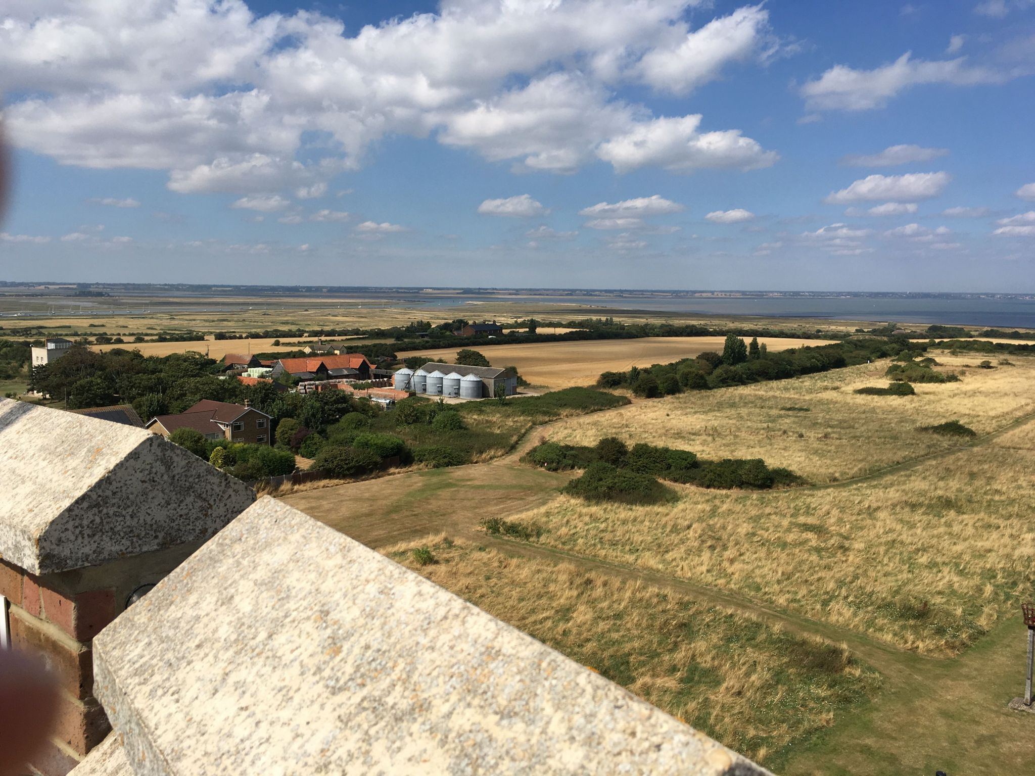 The view north from the top of the Naze Tower showing farmland and buildings, marshland, with the tip of The Naze, Hamford Water and the coastline heading towards Harwich