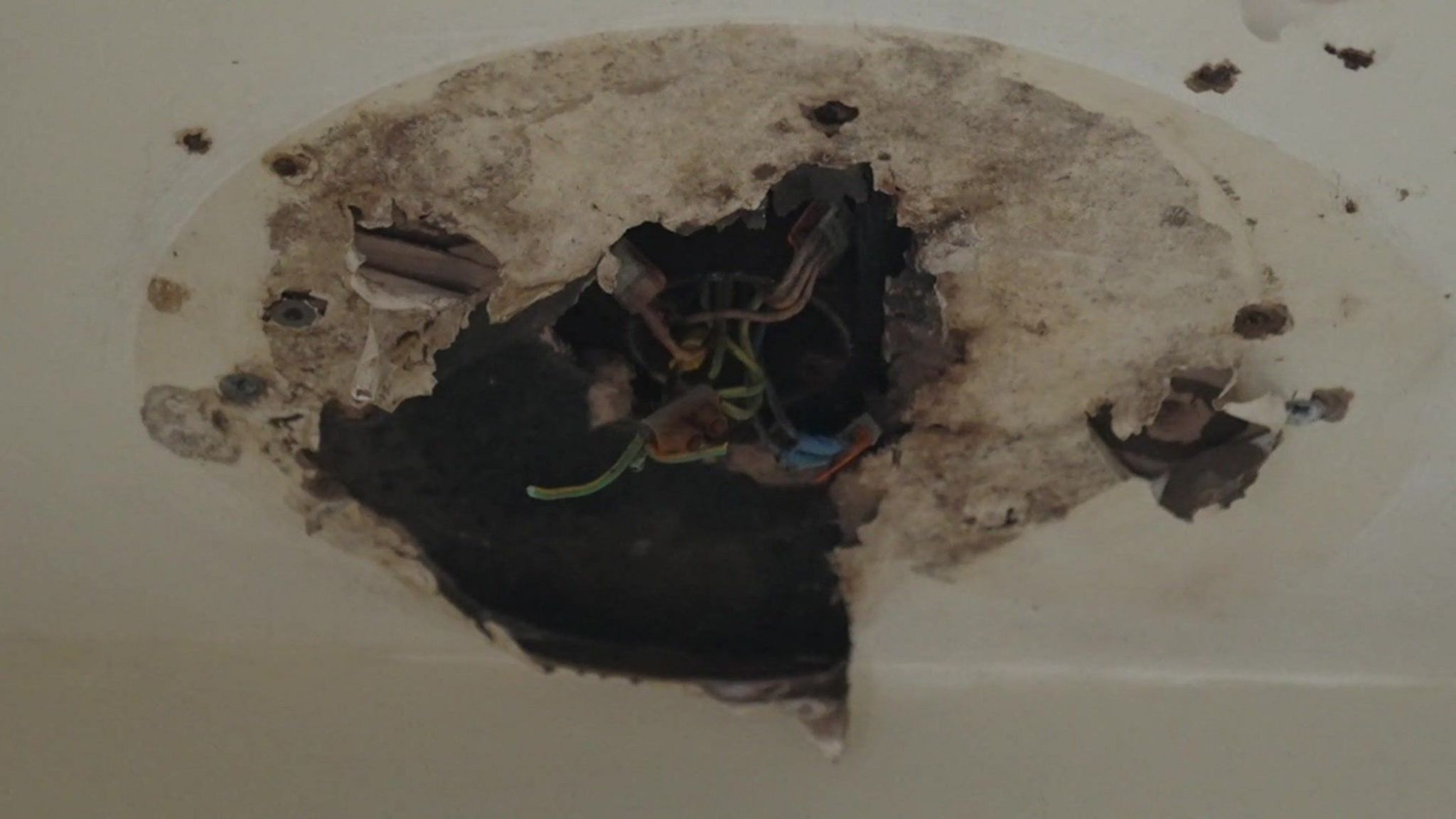 A hole in the ceiling of Ms Scott's toilet, with staining and exposed wiring