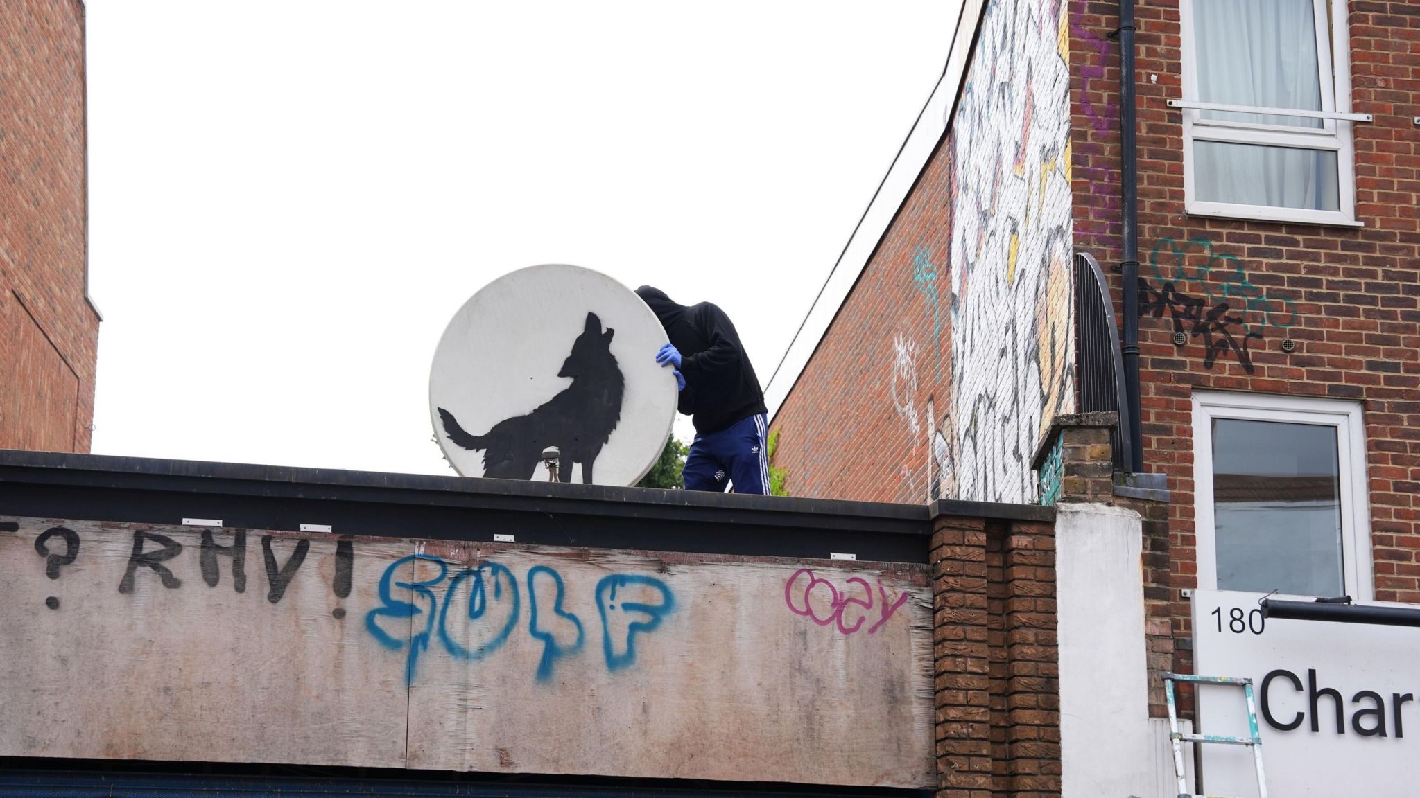 Someone removing the satellite dish featuring the Banksy artwork on it