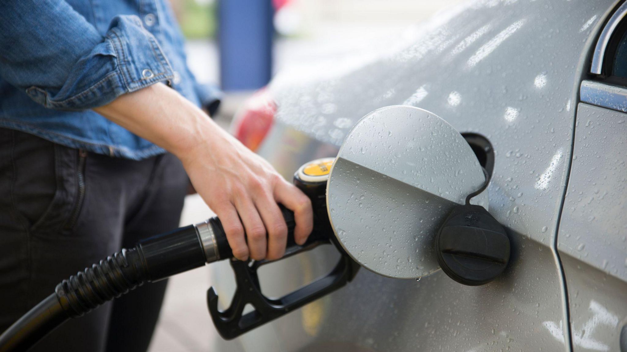 A woman holding a petrol pump as she refuels her car