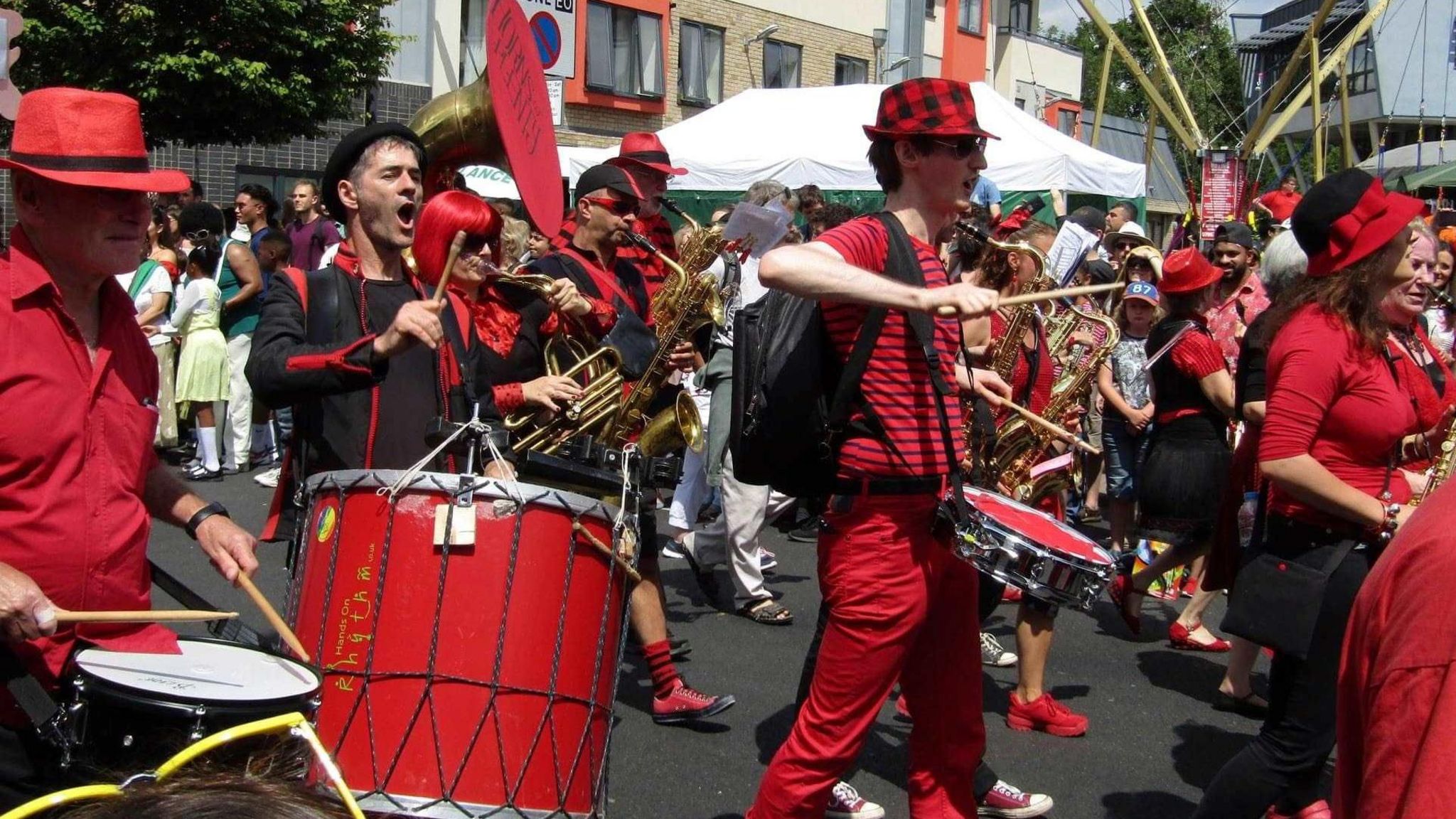 A steelband dressed in black and red playing instruments in the street