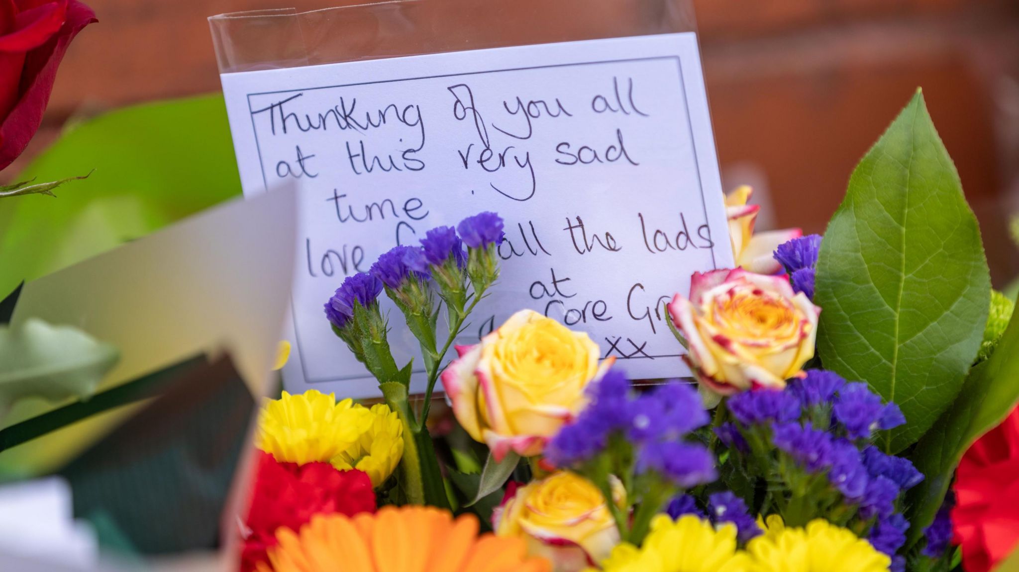 Purple, yellow and red flowers in a bouquet, with a message, reading: Thinking of you all at this very sad time