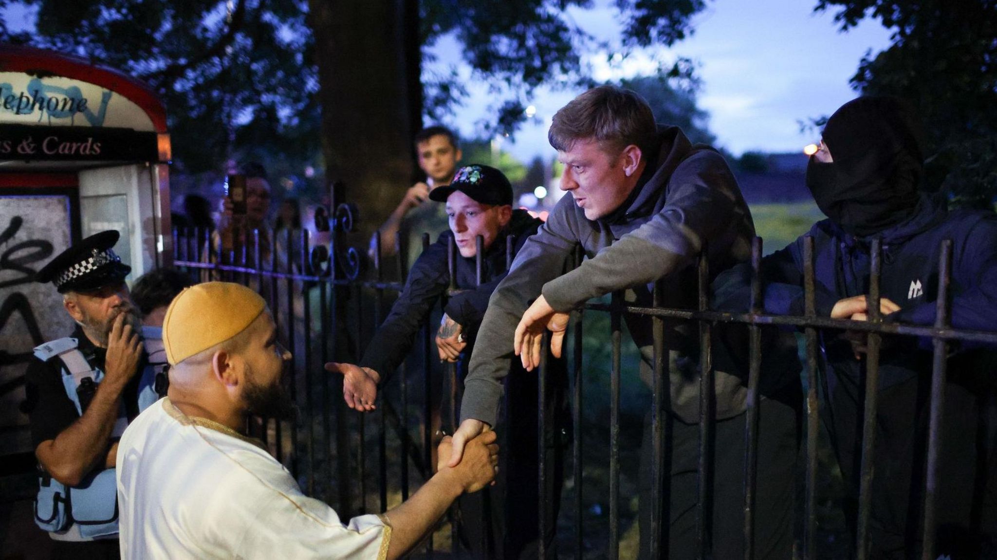 Protesters outside mosque shake hands with a worshipper, watched by a policeman