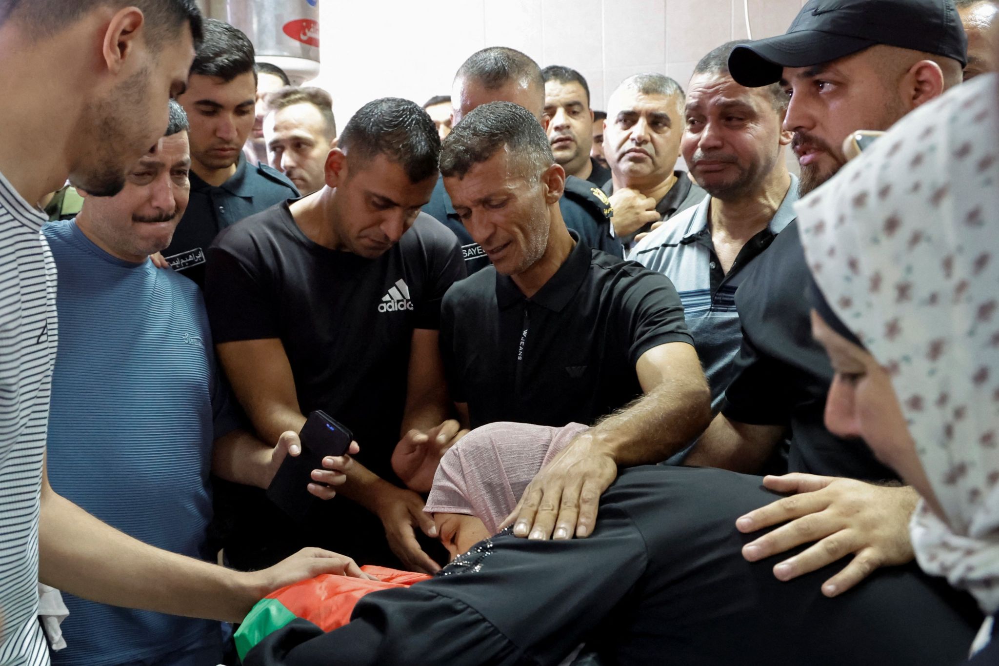 A woman lies on a corpse while others gather round at a funeral