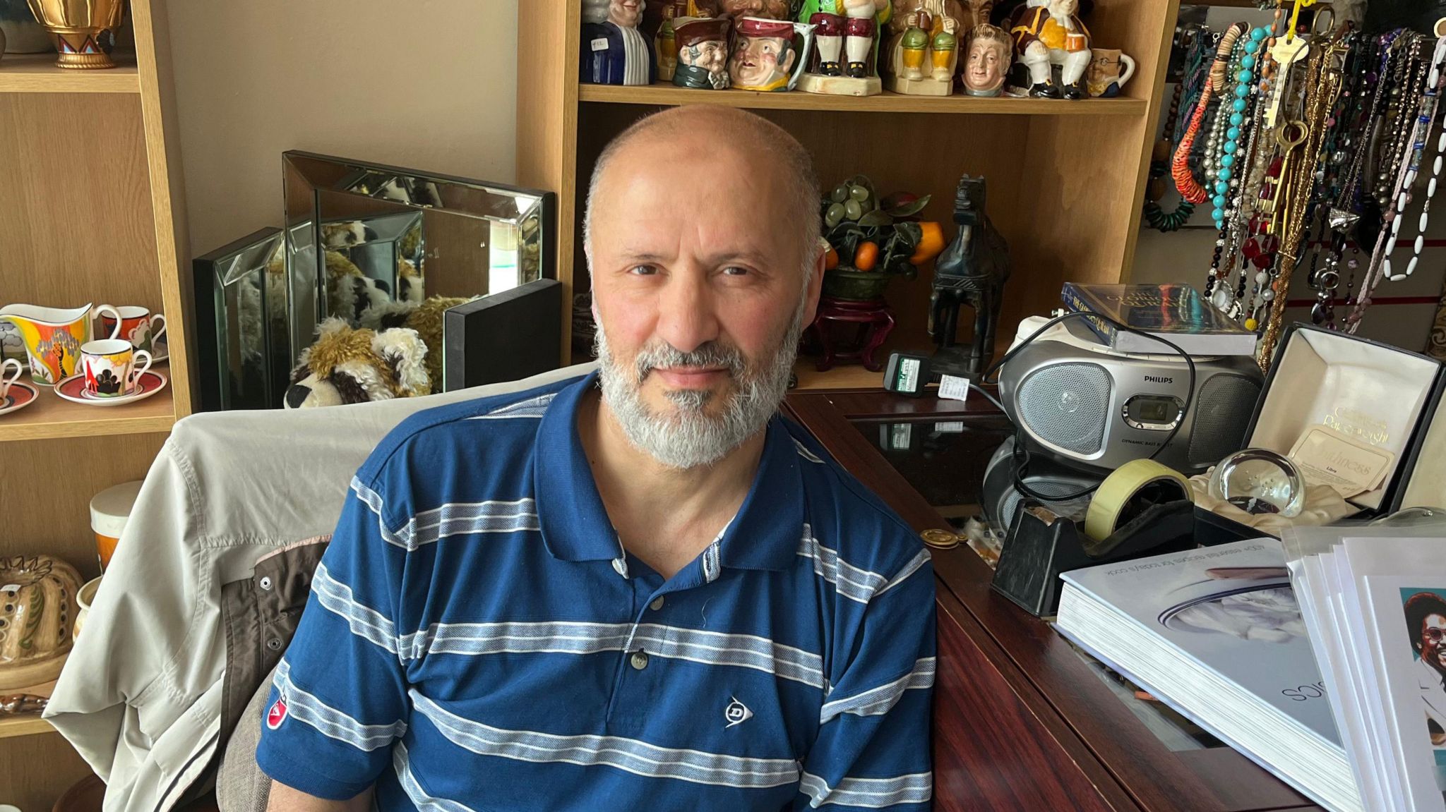 Fuad Akalach sitting at his desk in his antique shop. He is surrounded by antiques 