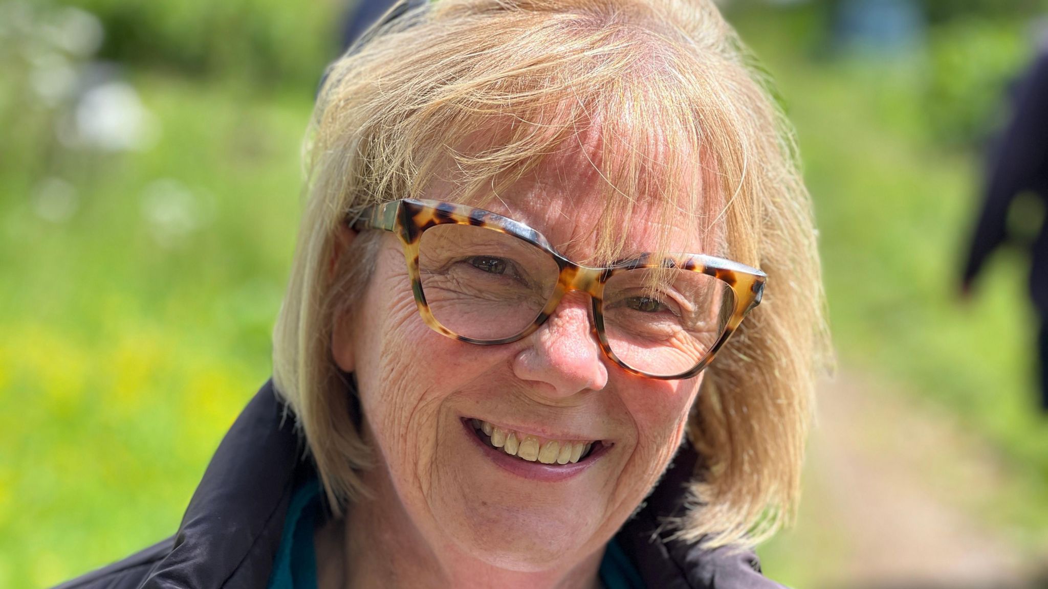 Close up portrait of Bernadette Knight wearing glasses and smiling as she stands in the allotments