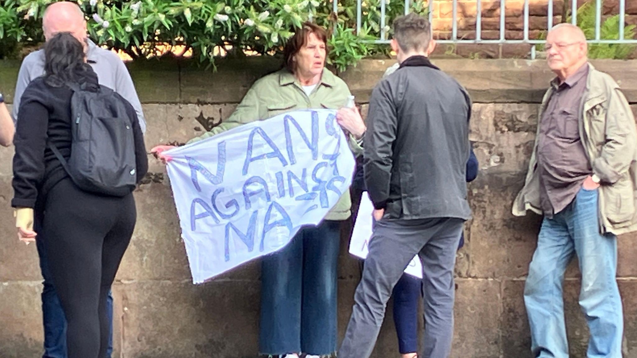 A lady holds a sign which reads Nans against Nazis as she leans against a wall in liverpool