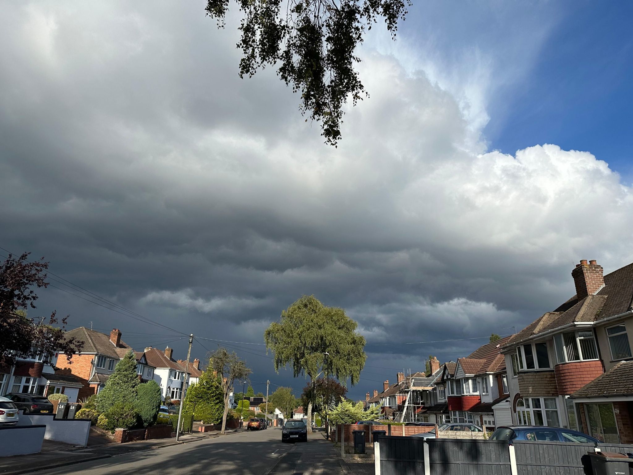 One corner of the shot shows blue sky, but thick black clouds are rolling across the rest of it, above a street of semi-detached houses from the early 20th Century.