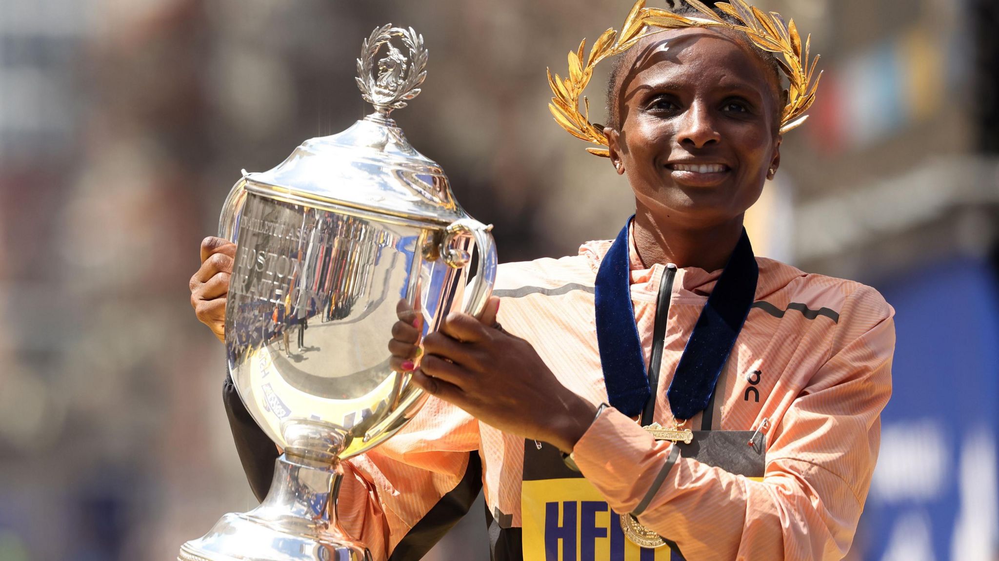 Hellen Obiri, wearing a laurel crown, poses with a trophy after winning the 2024 Boston Marathon