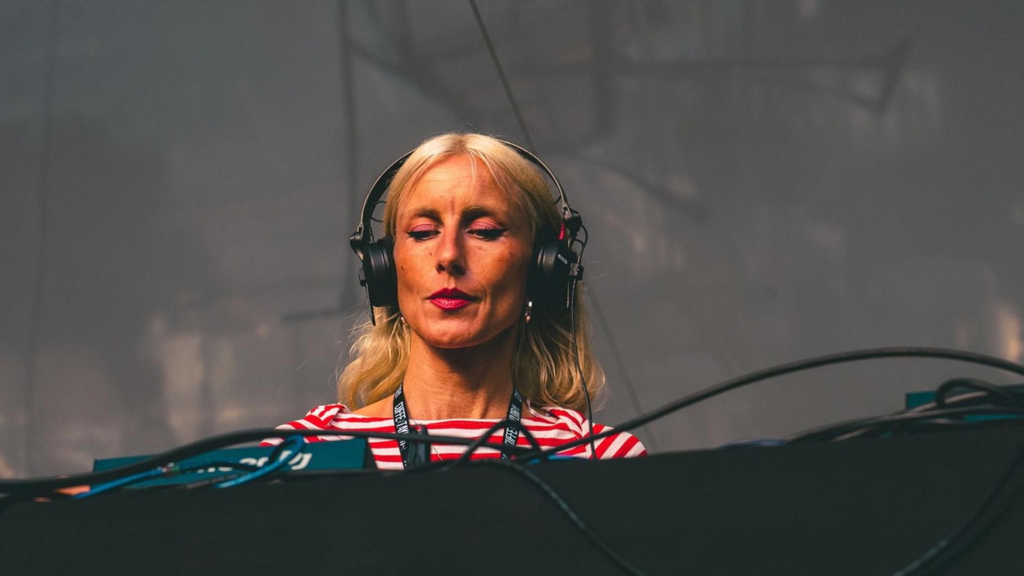 Blonde woman wearing a red and white stripe t shirt wears headphones at a DJ deck