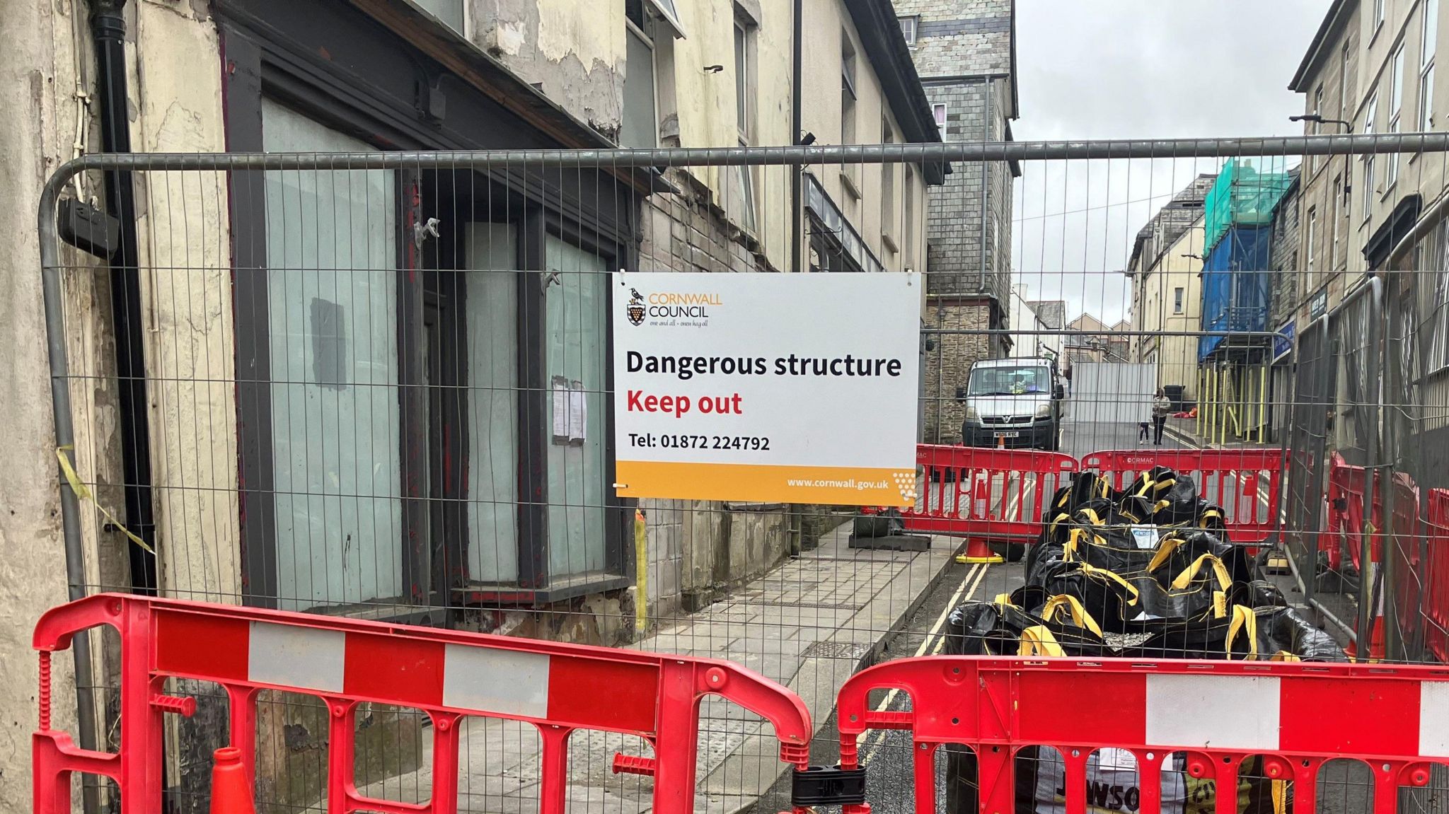 A cordoned off building with a fence going across the entire main road in Camelford. A sign says: "Dangerous Structure. Keep out."