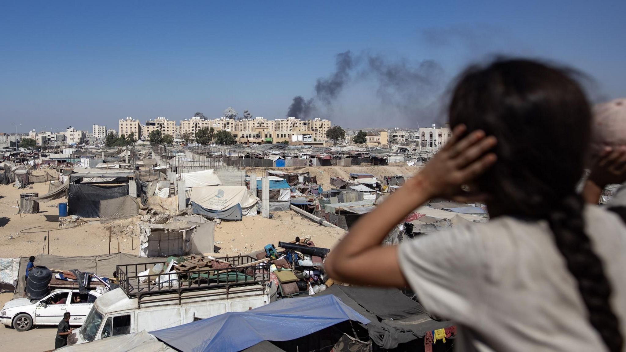 A Palestinian girl covers her ears as Israeli air strikes hit residential buildings  close to tents for displaced people in Khan Younis, in the southern Gaza Strip (16 August 2024)