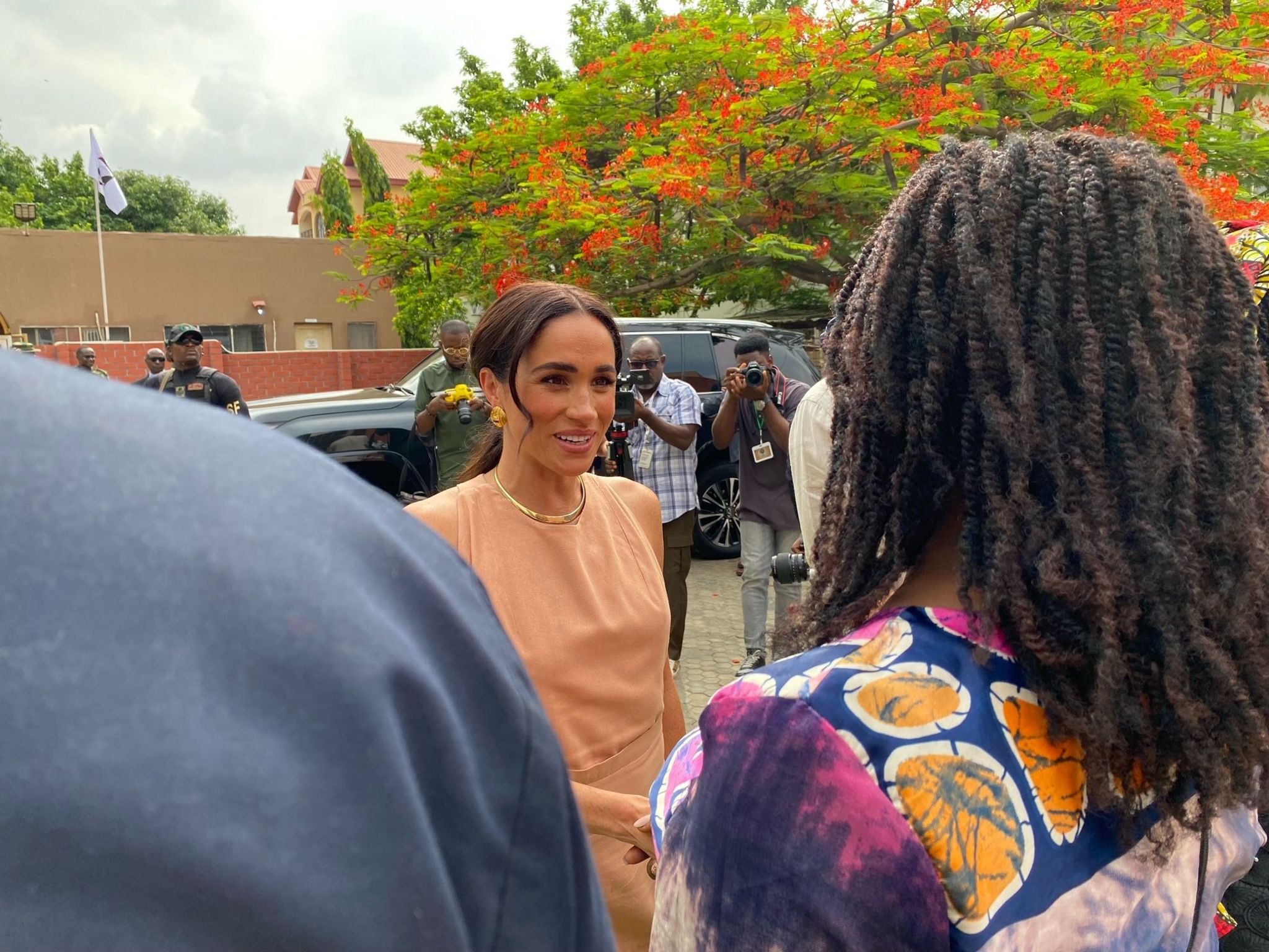 Meghan Duchess of Sussex greeting two people with a line of photographers behind her