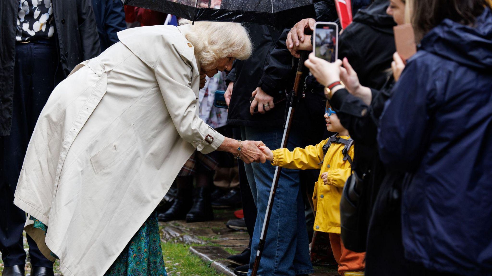 Queen Camilla meeting a young boy in a yellow rain coat