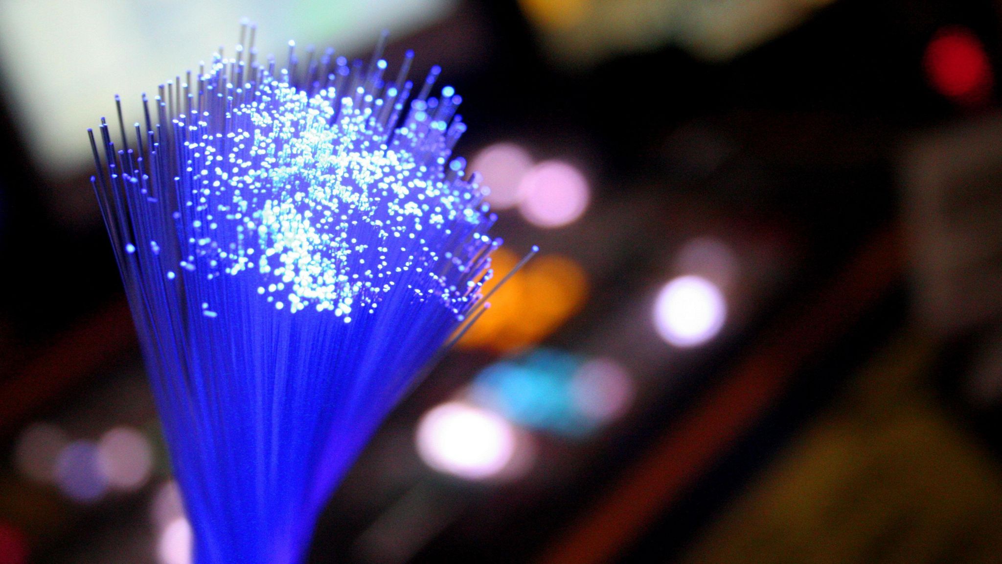 A bundle of fibre optic cables illuminated in blue with other blurred lights visible in the background