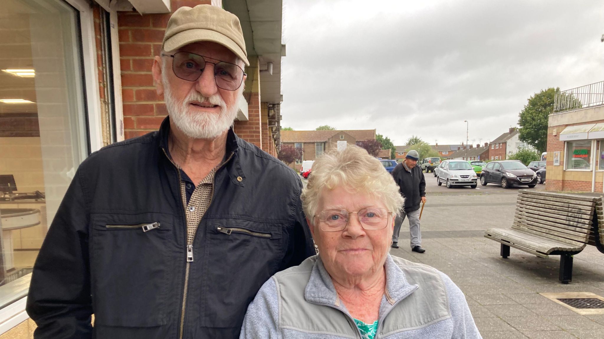 Michael and Tessa Crayford, an elderly couple wearing jackets, standing outside