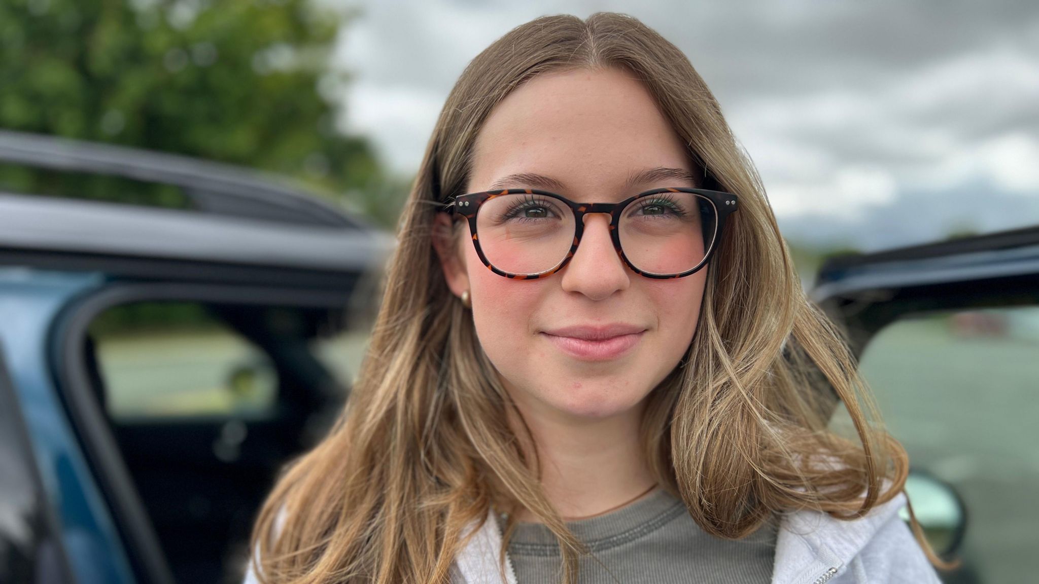 A smiling Sara Canamares looking directly into the camera, wearing brown glasses