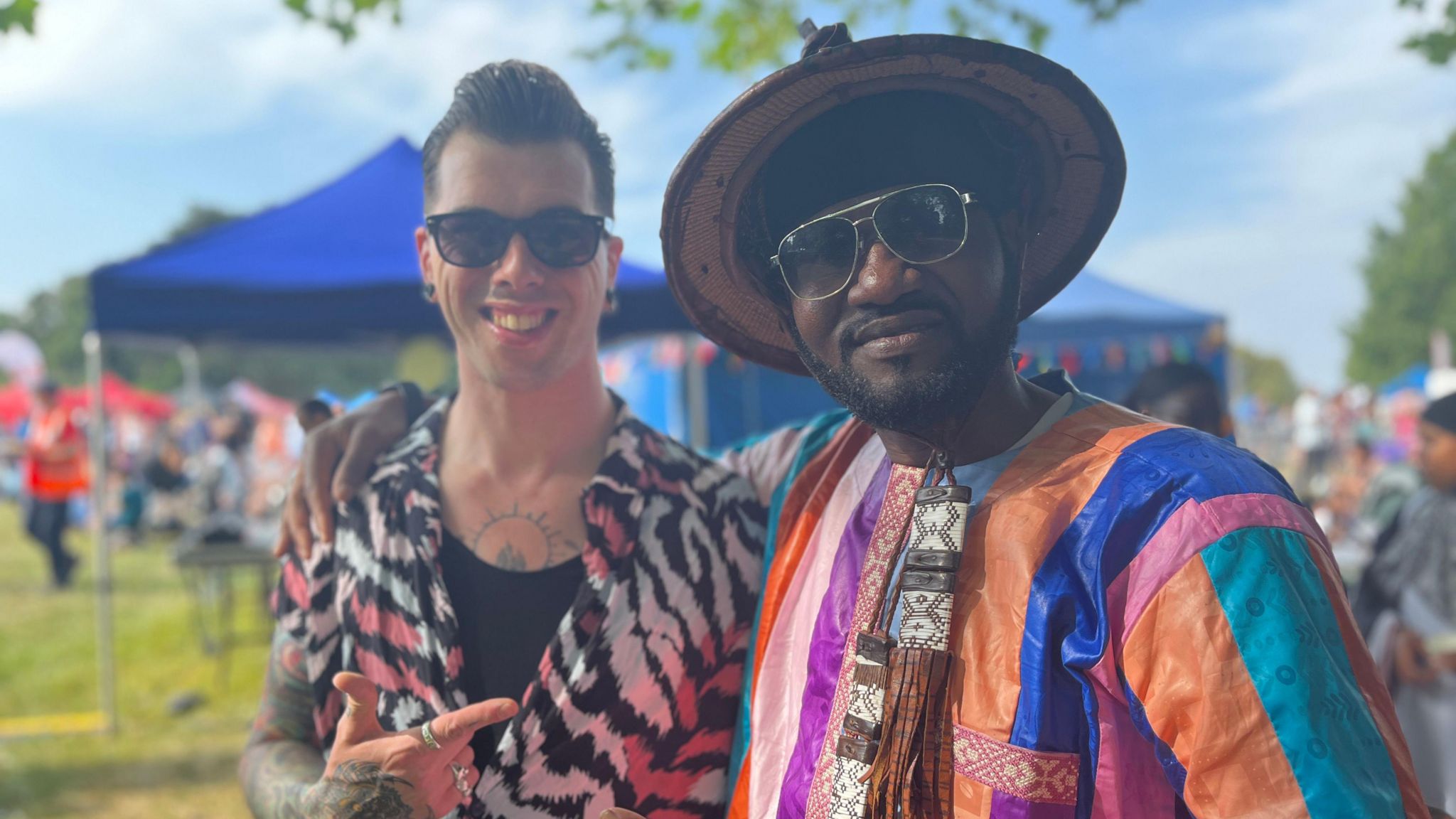 Josh Locke, a white man with 1950's style hair, has his arm around Loko Lomal, a black man in a colourful Senegalese shirt and straw hat