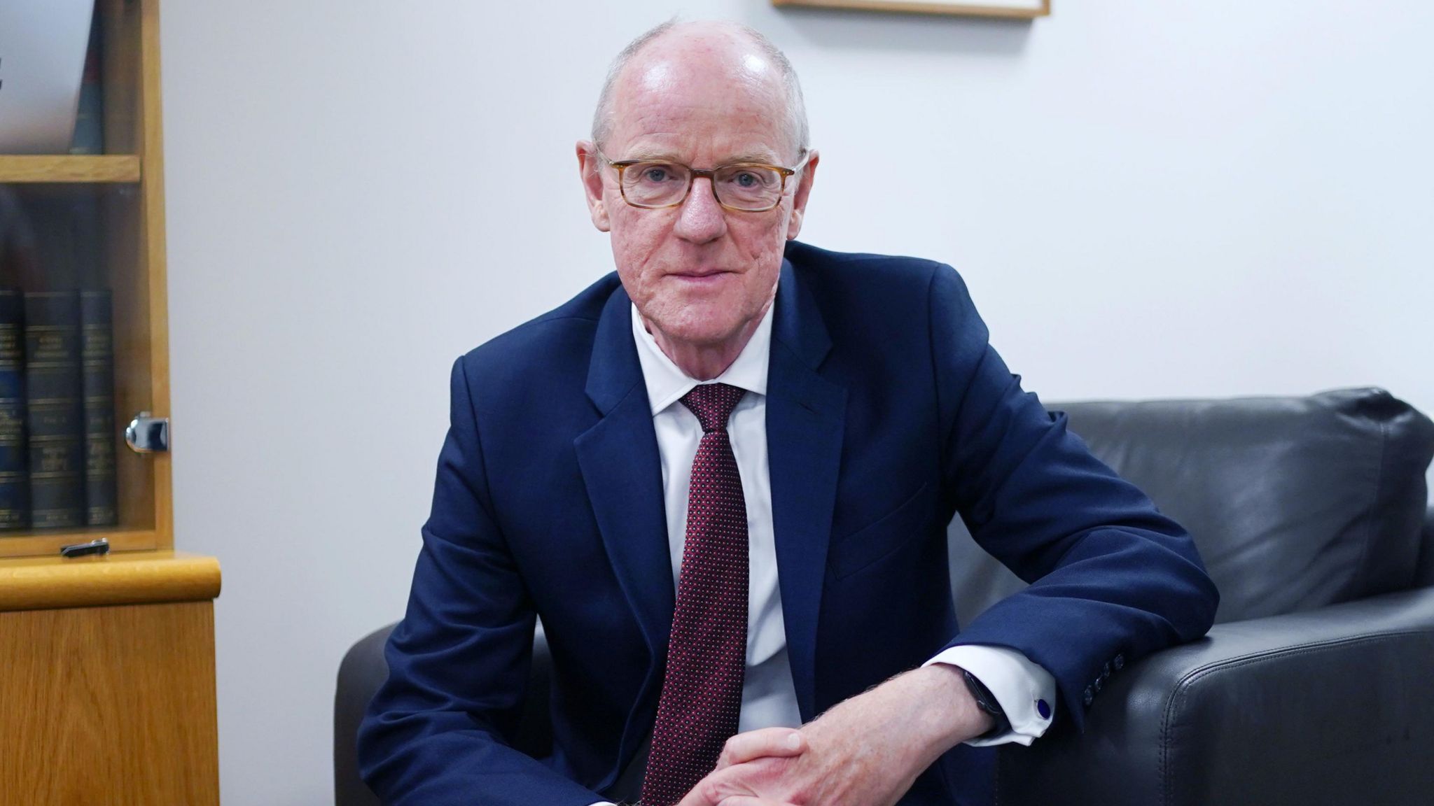 Nick Gibb sitting in a leather chair wearing glasses and a suit