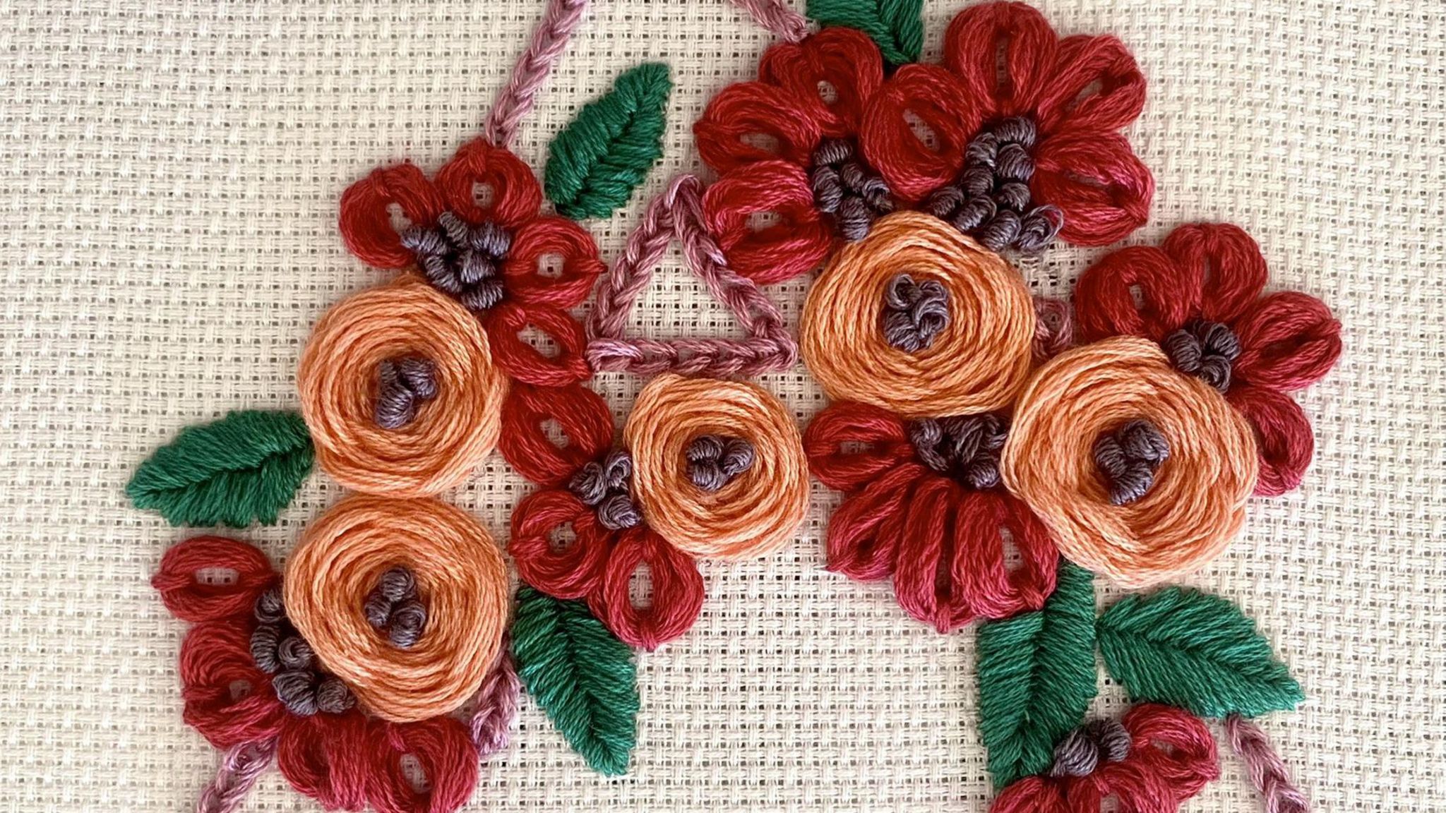 A piece of embroidery mad e up of orange and red flowers with green leaves