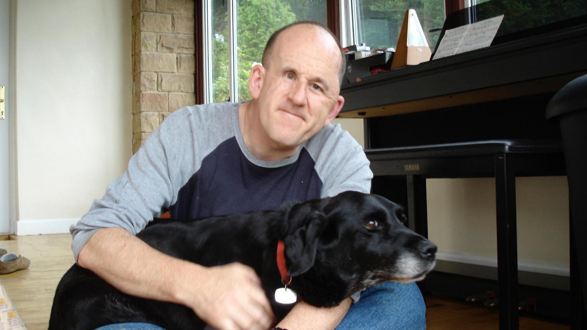 A middle aged man with cropped hair hugs a large black dog