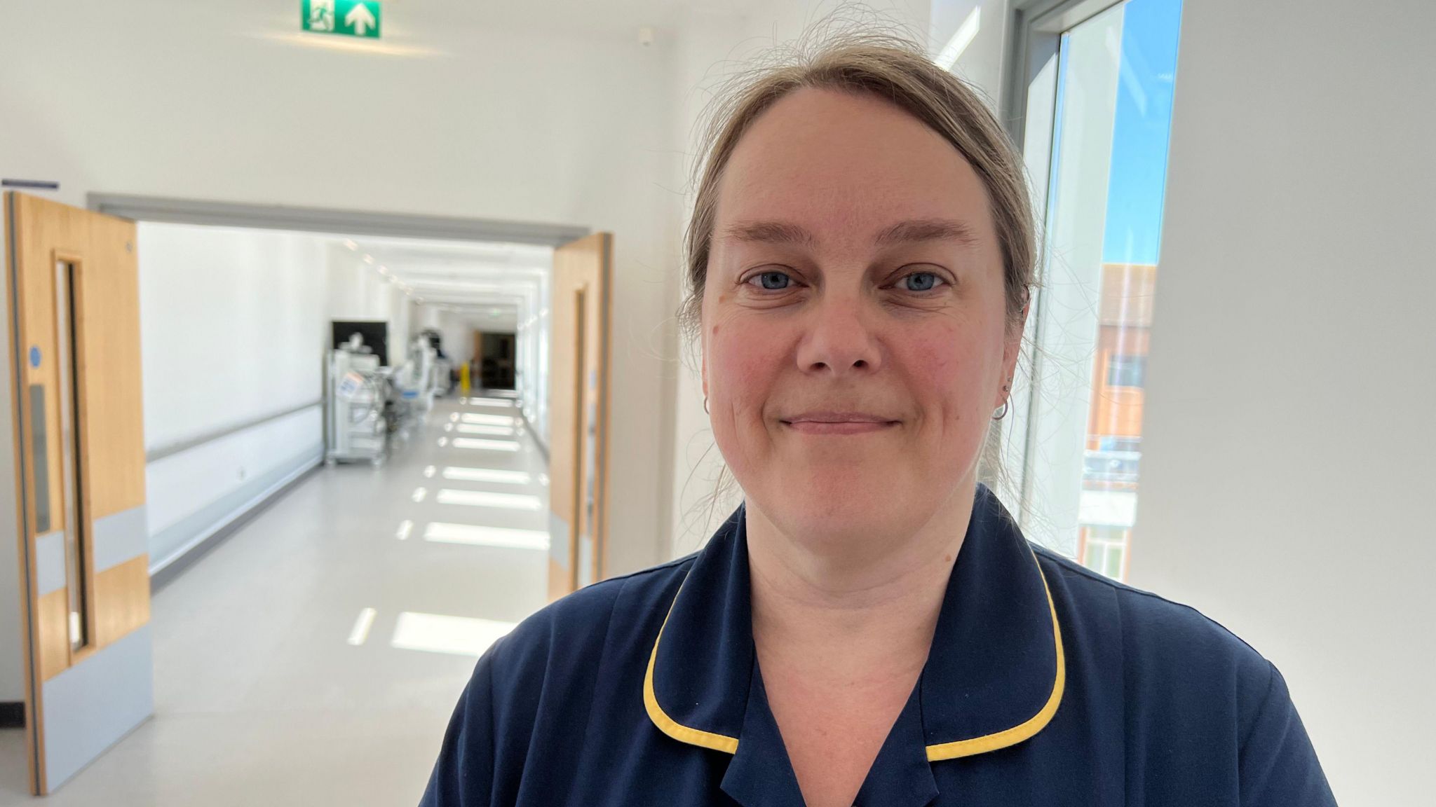 Zoe Hall in a hospital corridor. She is wearing blue and yellow nurse uniform